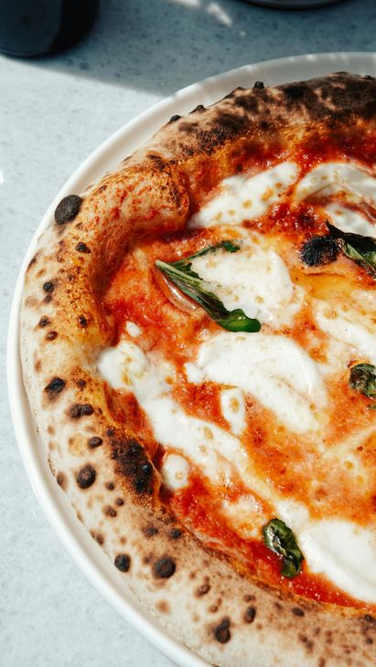 Primo piano di una pizza Margherita con formaggio fuso, salsa di pomodoro e basilico su un piatto