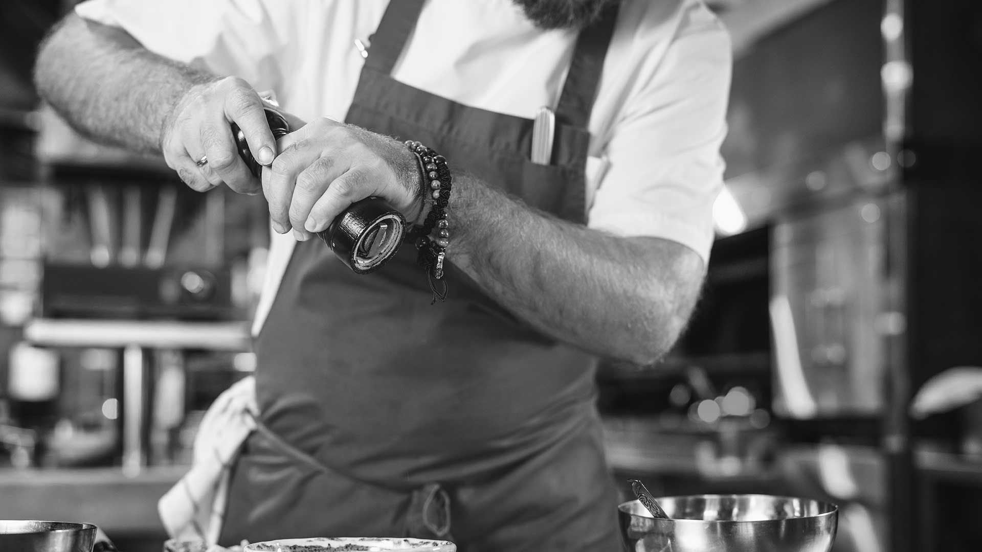 A photograph of a man in an apron with a pepper grinder