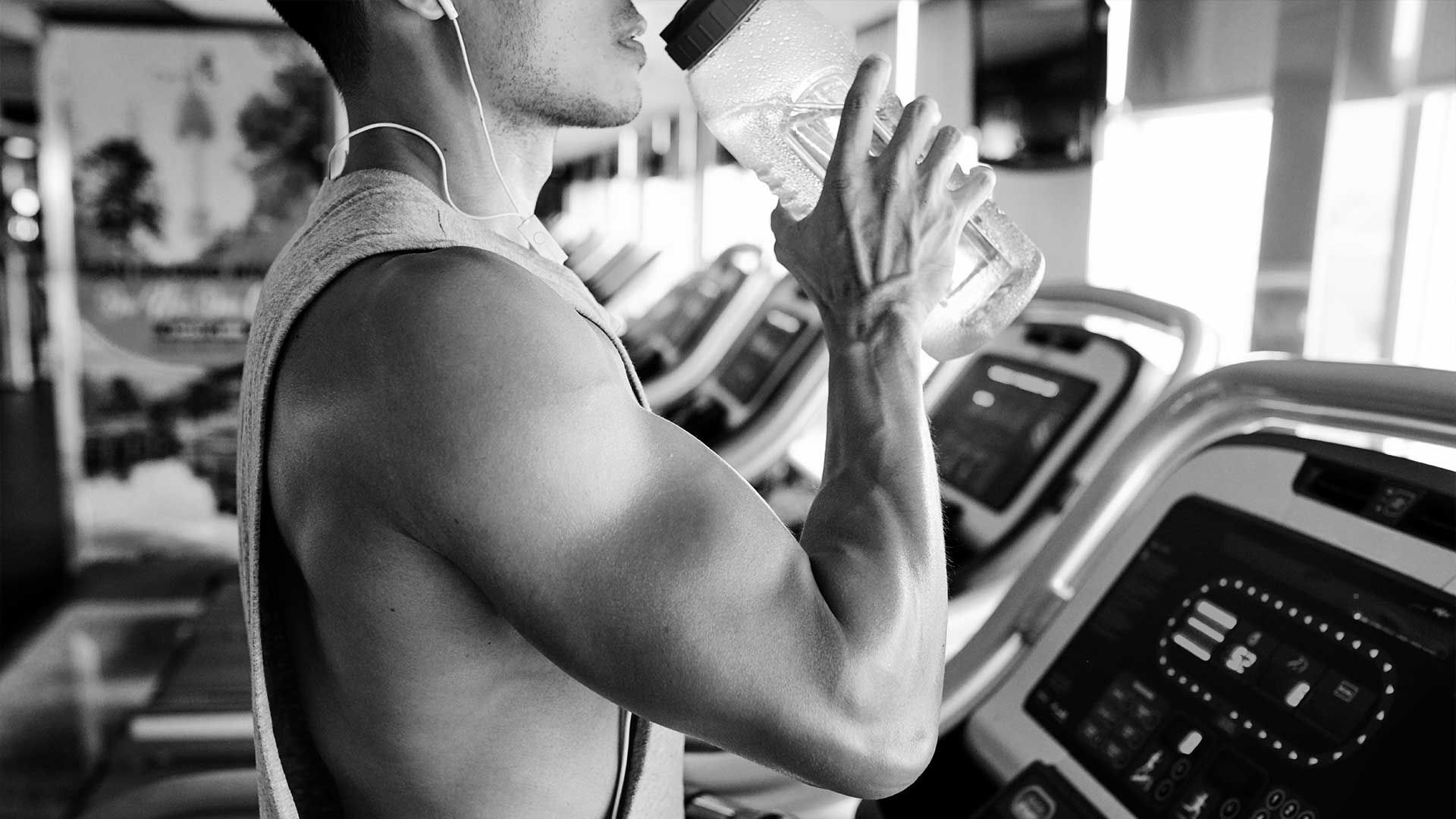 A man is drinking water from a bottle in a gym.