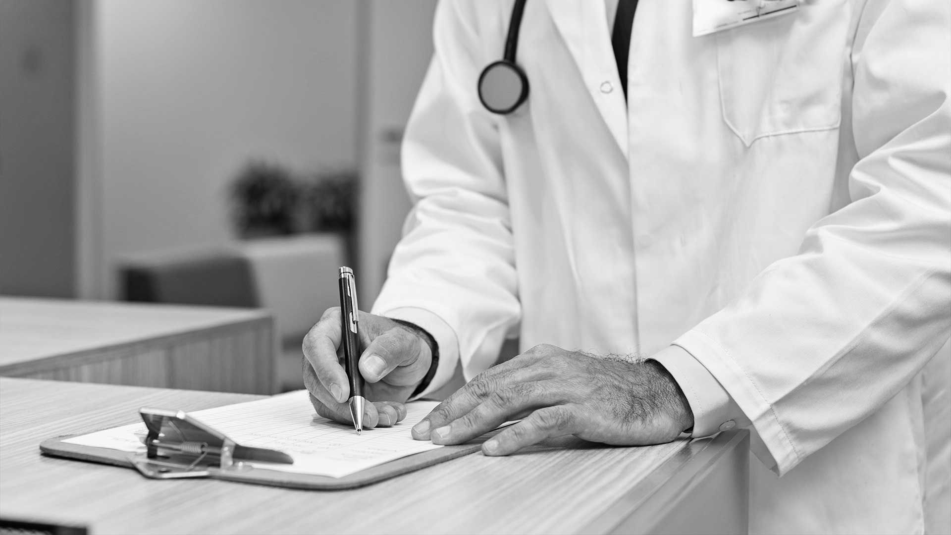 A doctor is writing on a clipboard in a black and white photo.