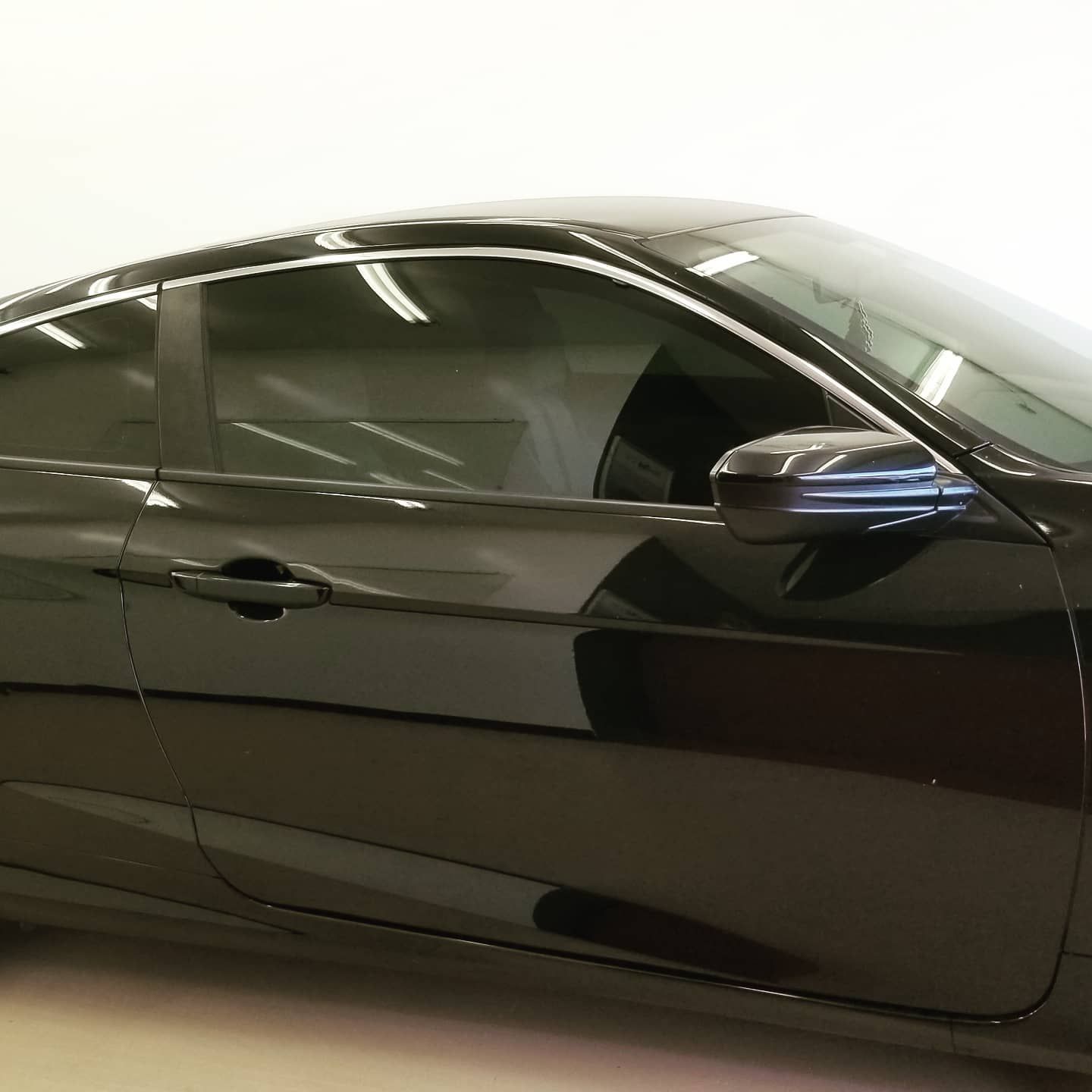 Black coupe car in a white studio, with tinted windows and a shiny exterior.