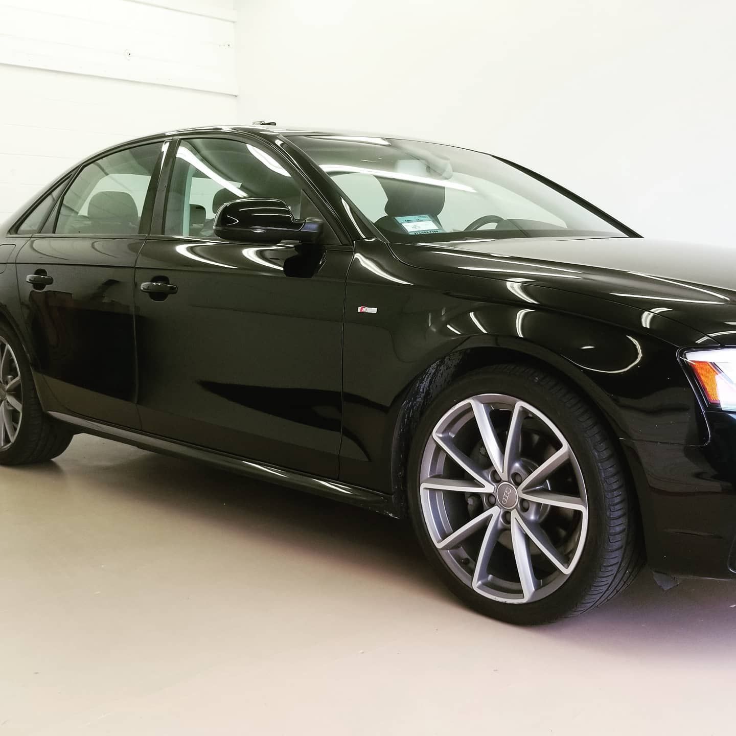 Black Audi sedan parked inside a brightly lit garage, showing off its shiny finish.