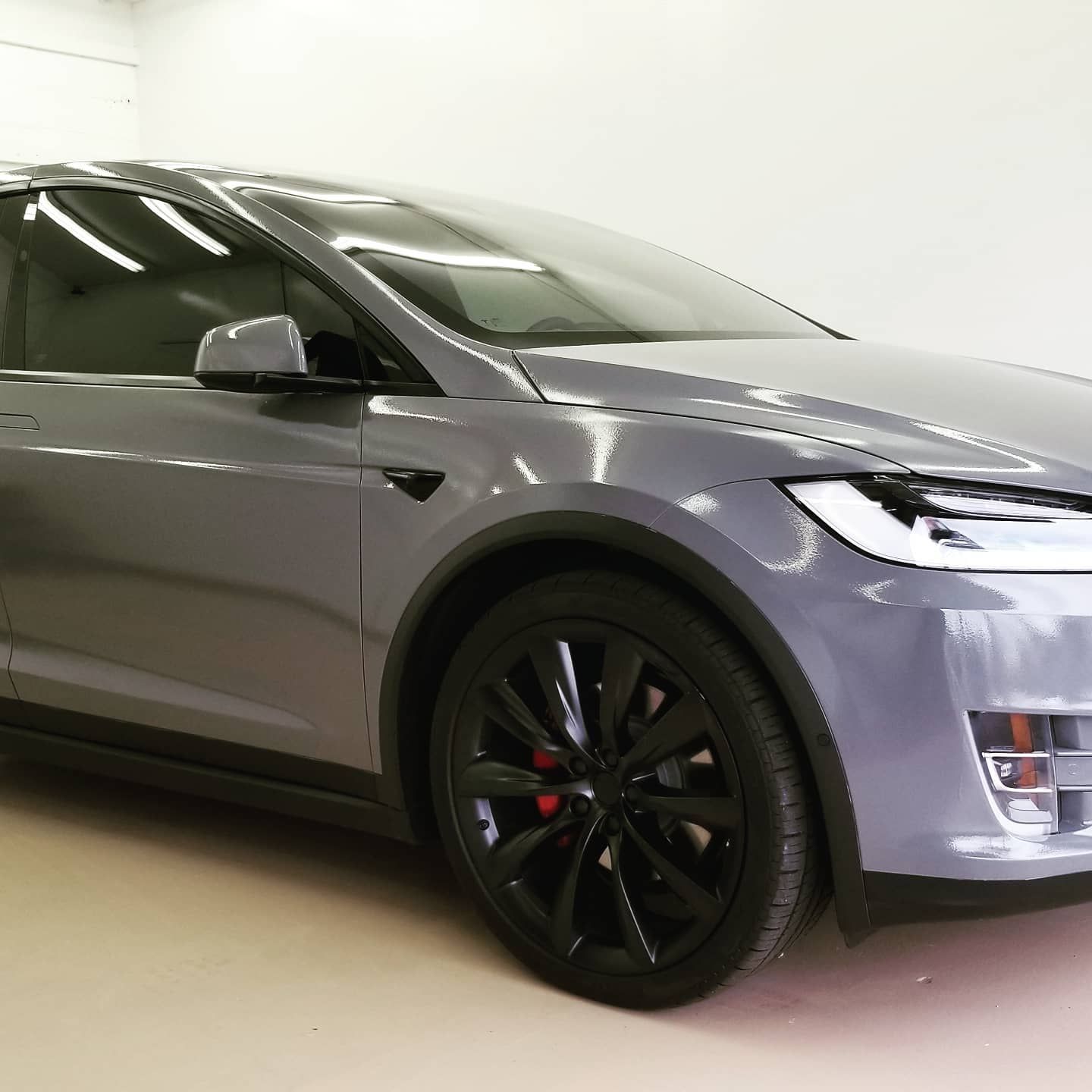 Gray Tesla Model X with black rims in a brightly lit studio.