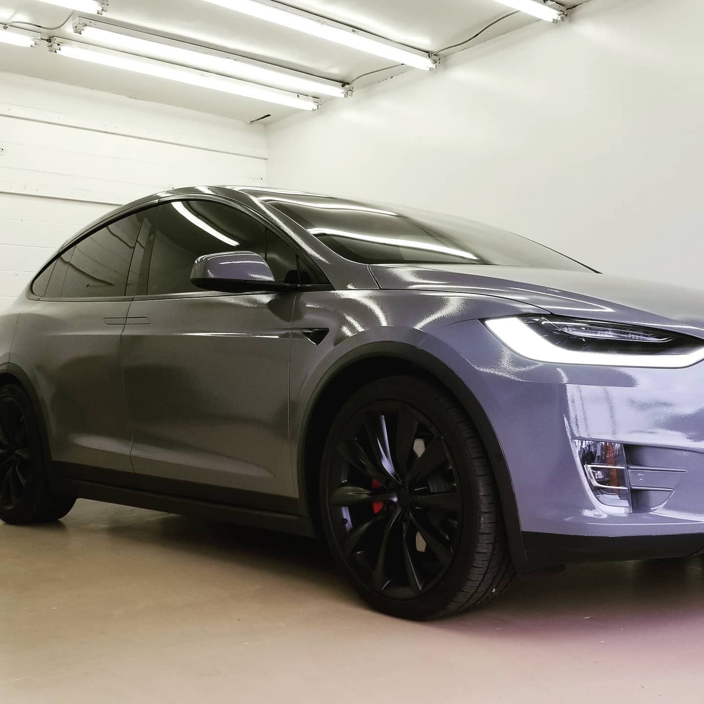 A gray Tesla Model X parked inside a well-lit garage. Black wheels and trim.