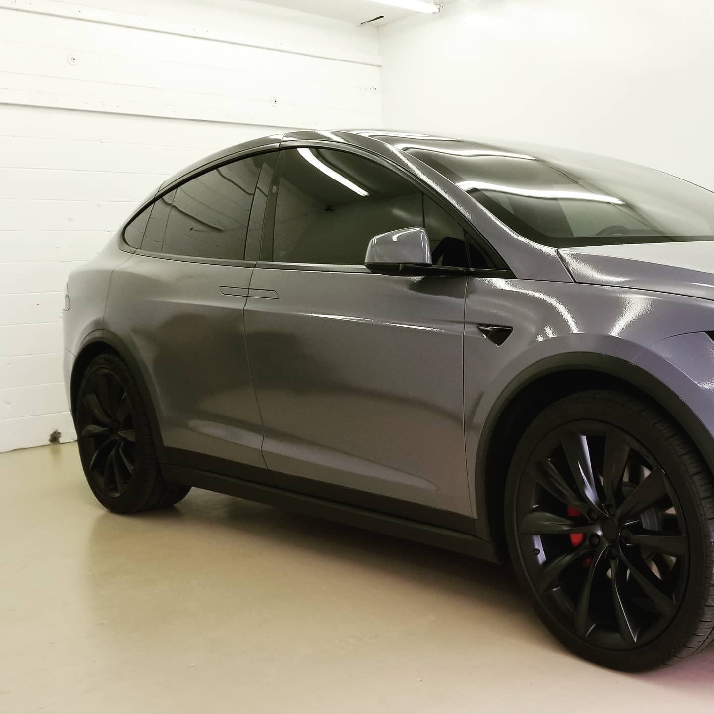Gray Tesla Model X with black wheels in a white-walled garage.