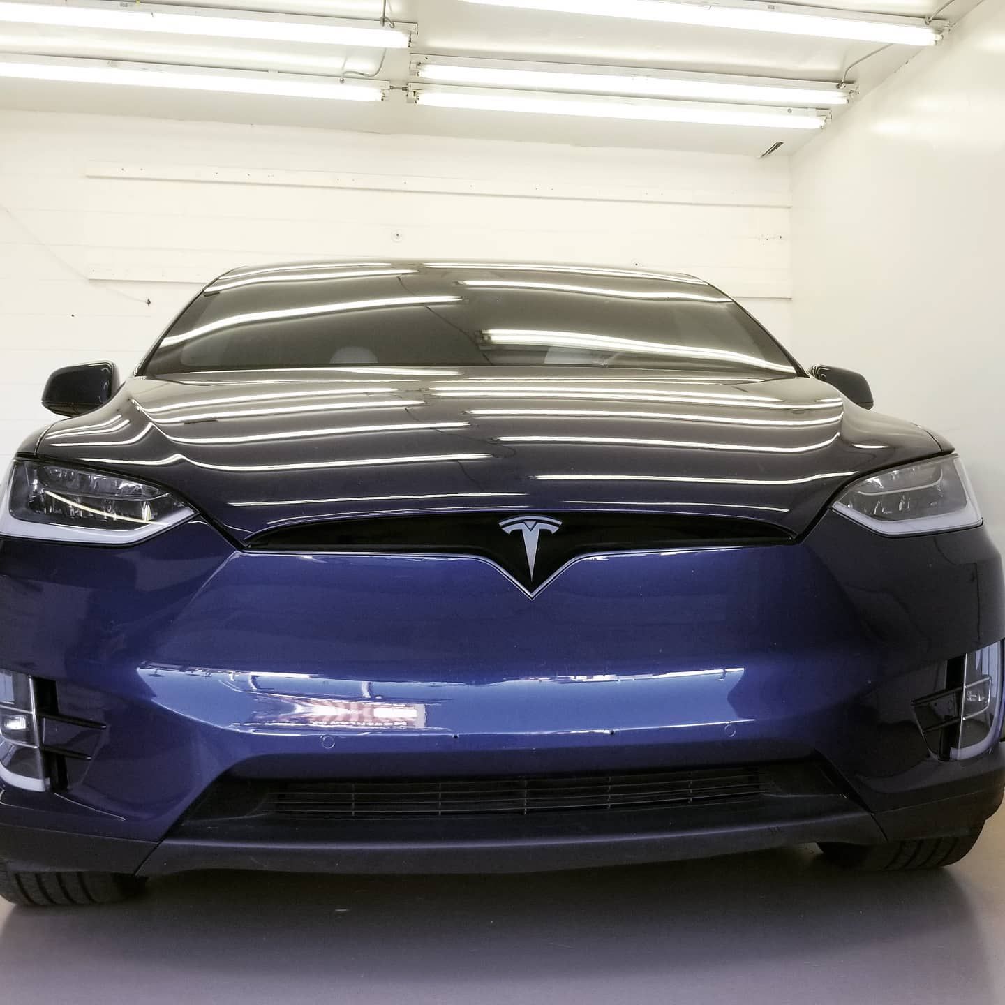 Blue Tesla Model X car parked indoors under bright lights.