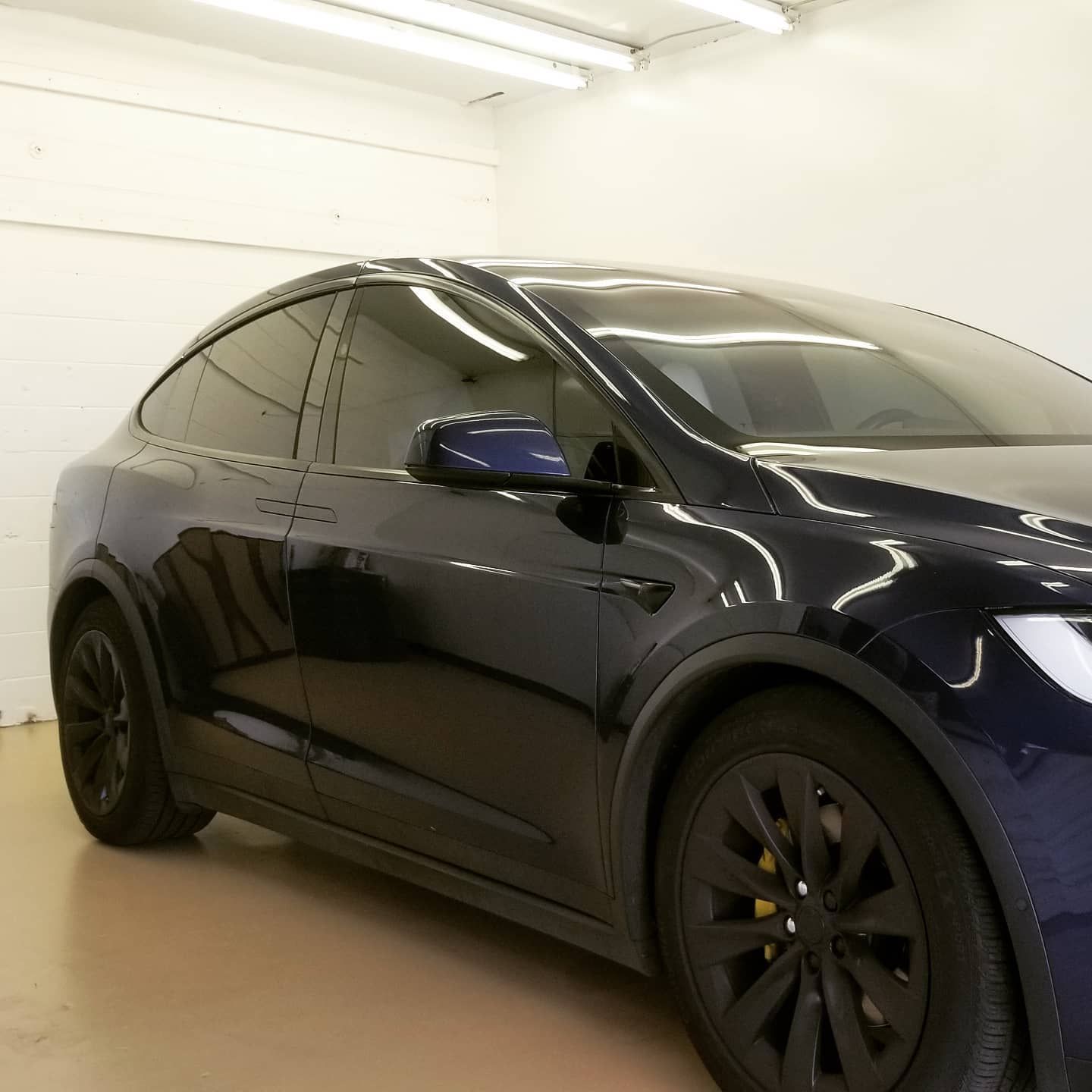 Dark blue Tesla Model X, black rims, parked indoors.