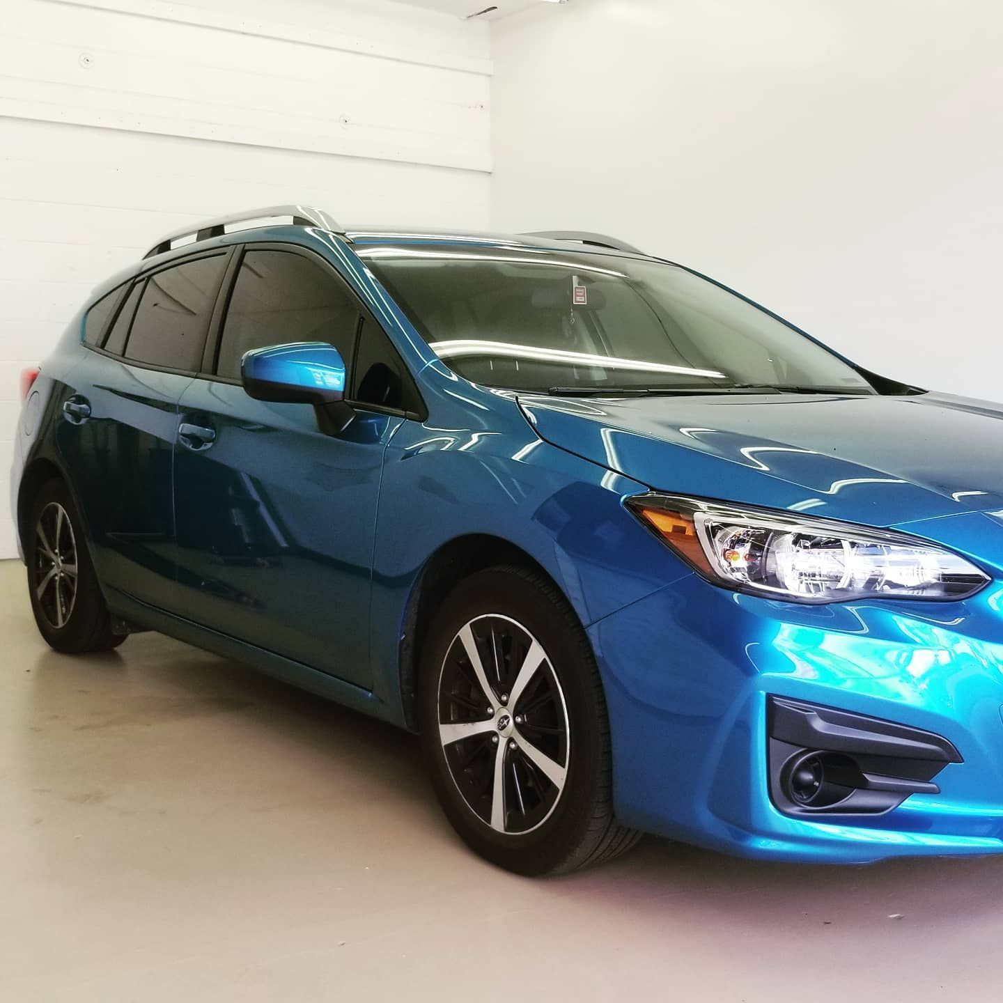 Blue Subaru Impreza hatchback with black wheels and roof rack, parked in a well-lit garage.