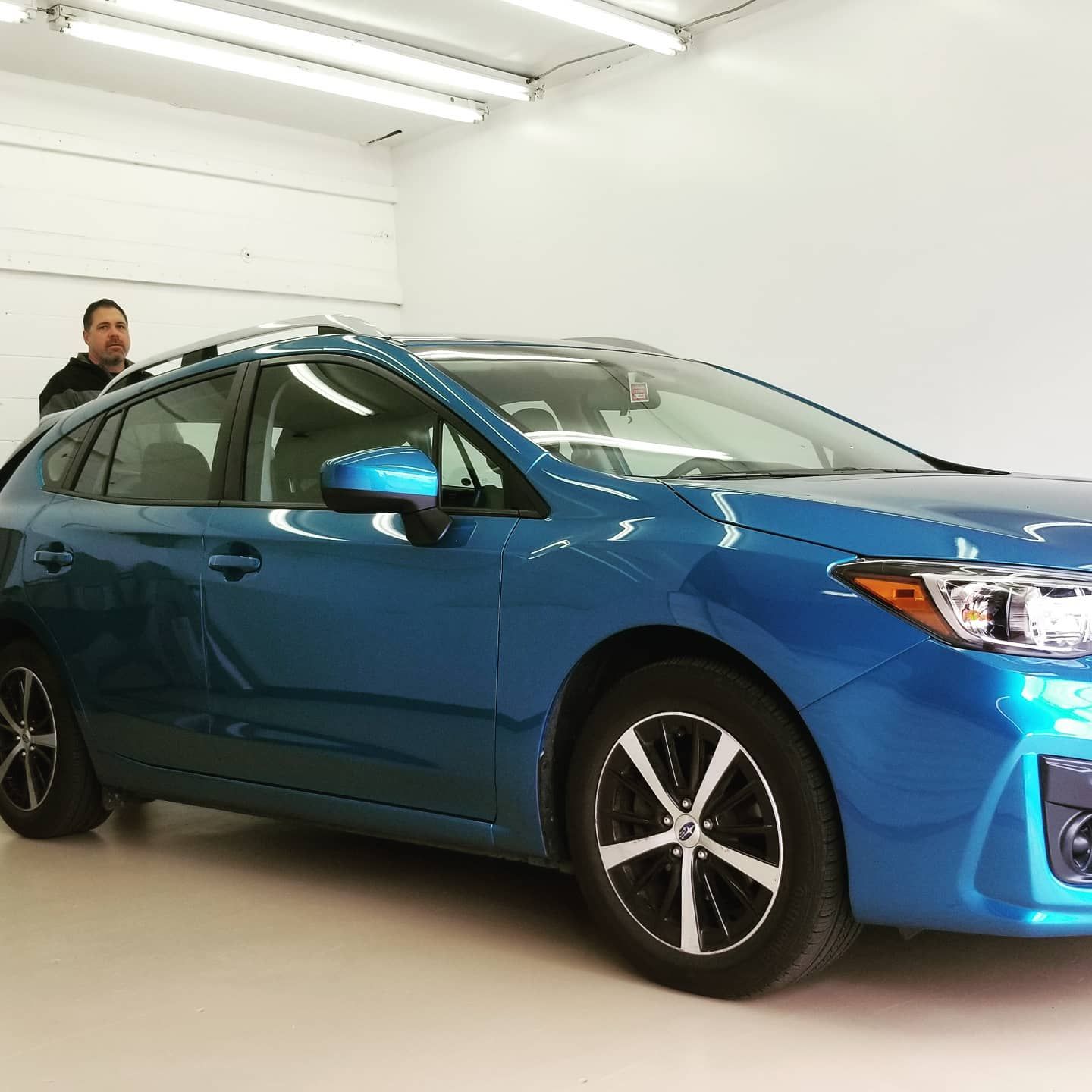 Blue Subaru in a brightly lit garage with a man standing by it.