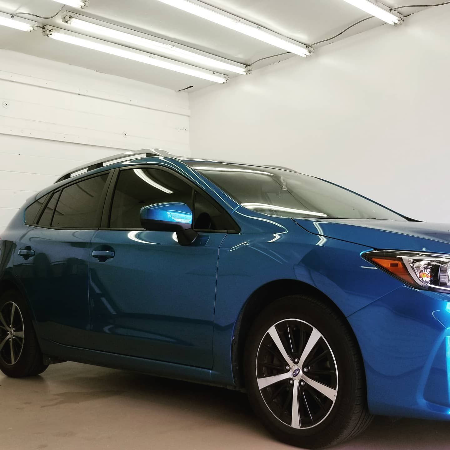 Blue Subaru hatchback in a brightly lit garage.