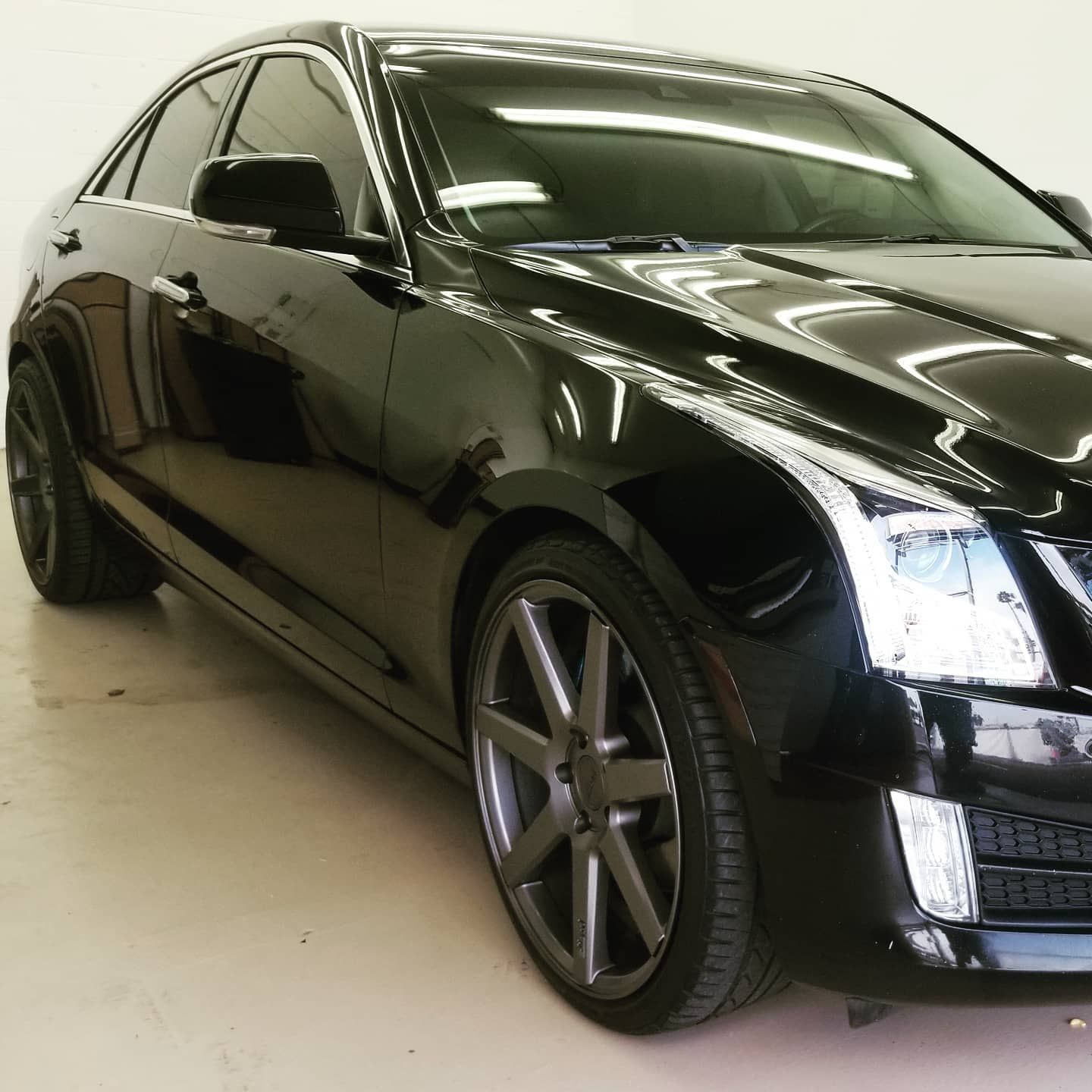 Black Cadillac sedan with gray rims, parked indoors.