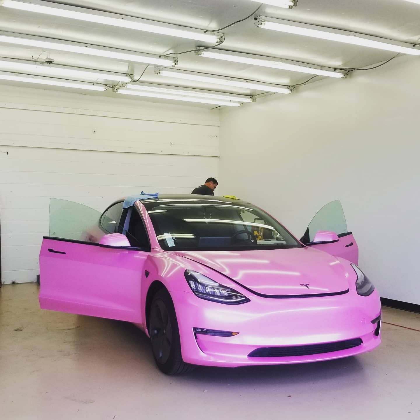 Pink Tesla being worked on inside a garage; doors open, person working.