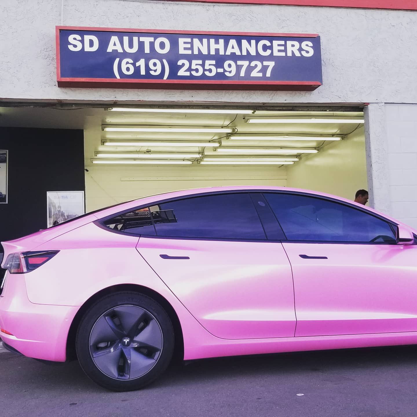 Pink Tesla car parked in front of SD Auto Enhancers shop. Phone number (619) 255-9727 is on the sign.