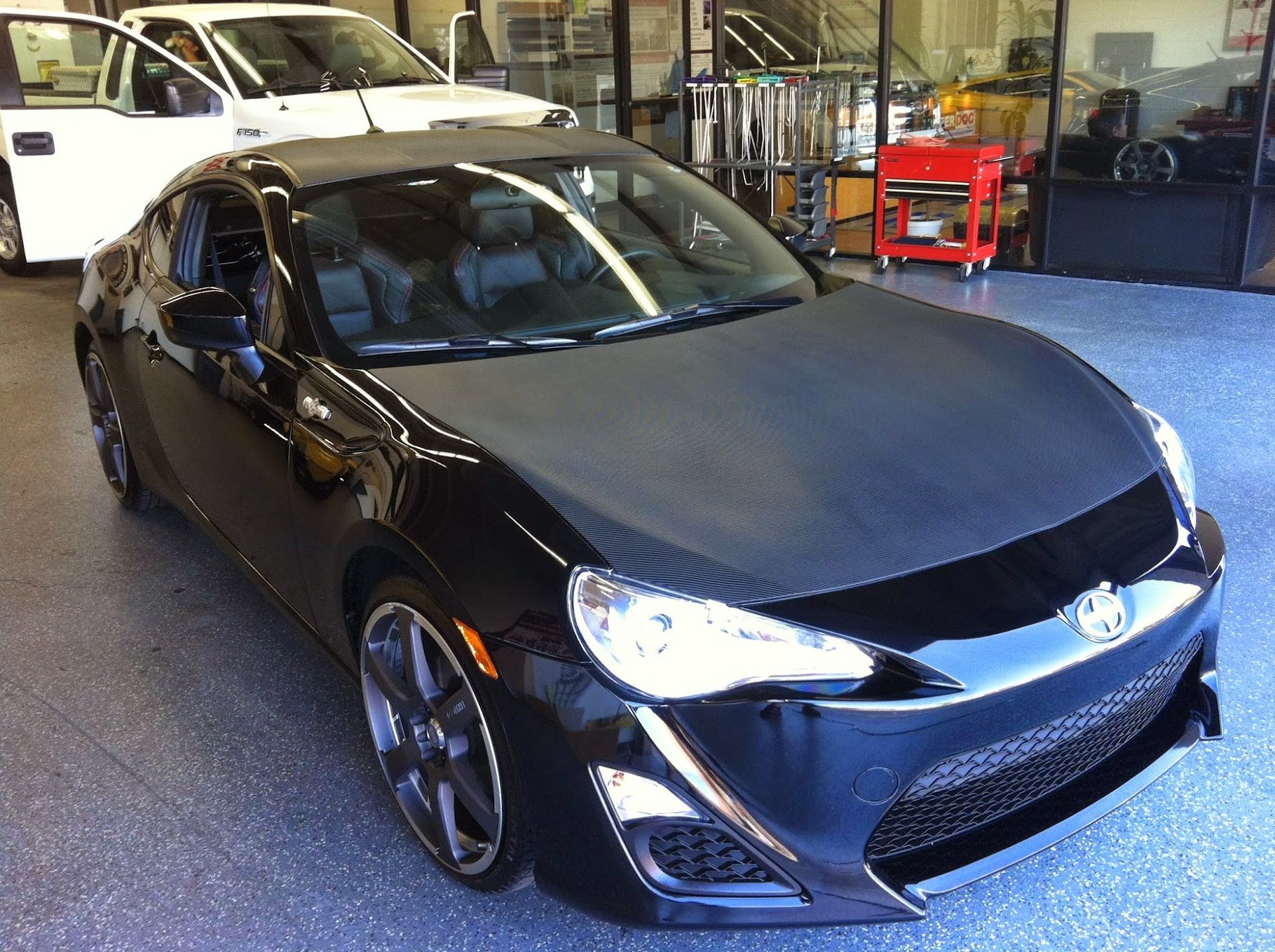 Black sports car with carbon fiber hood in a garage.