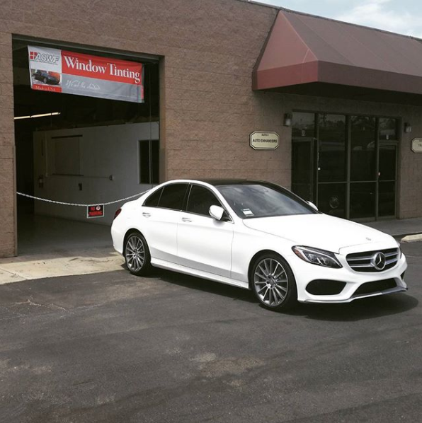 White Mercedes sedan parked outside a window tinting shop.