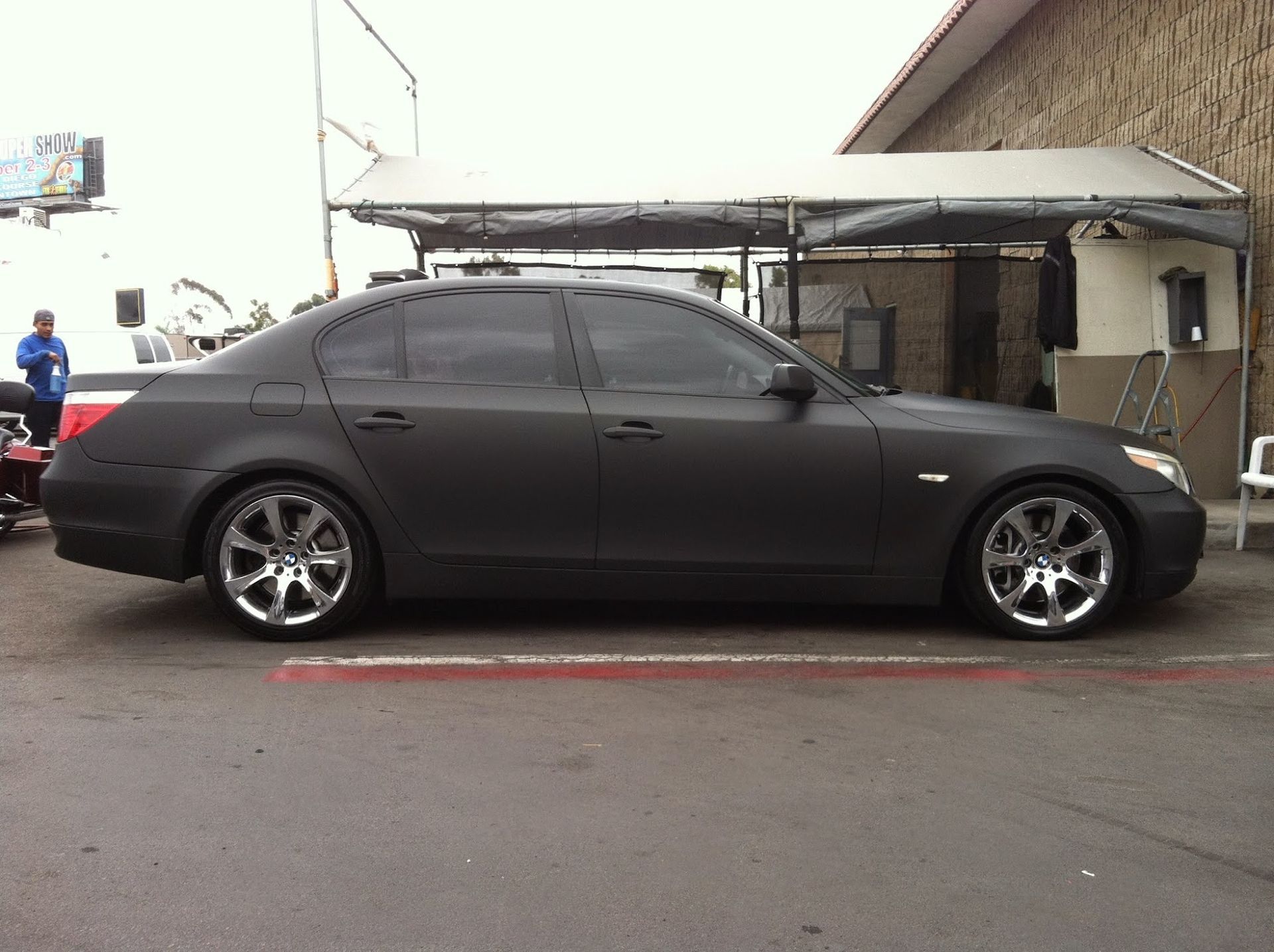 Black matte BMW sedan parked, chrome wheels, tinted windows, outdoors.