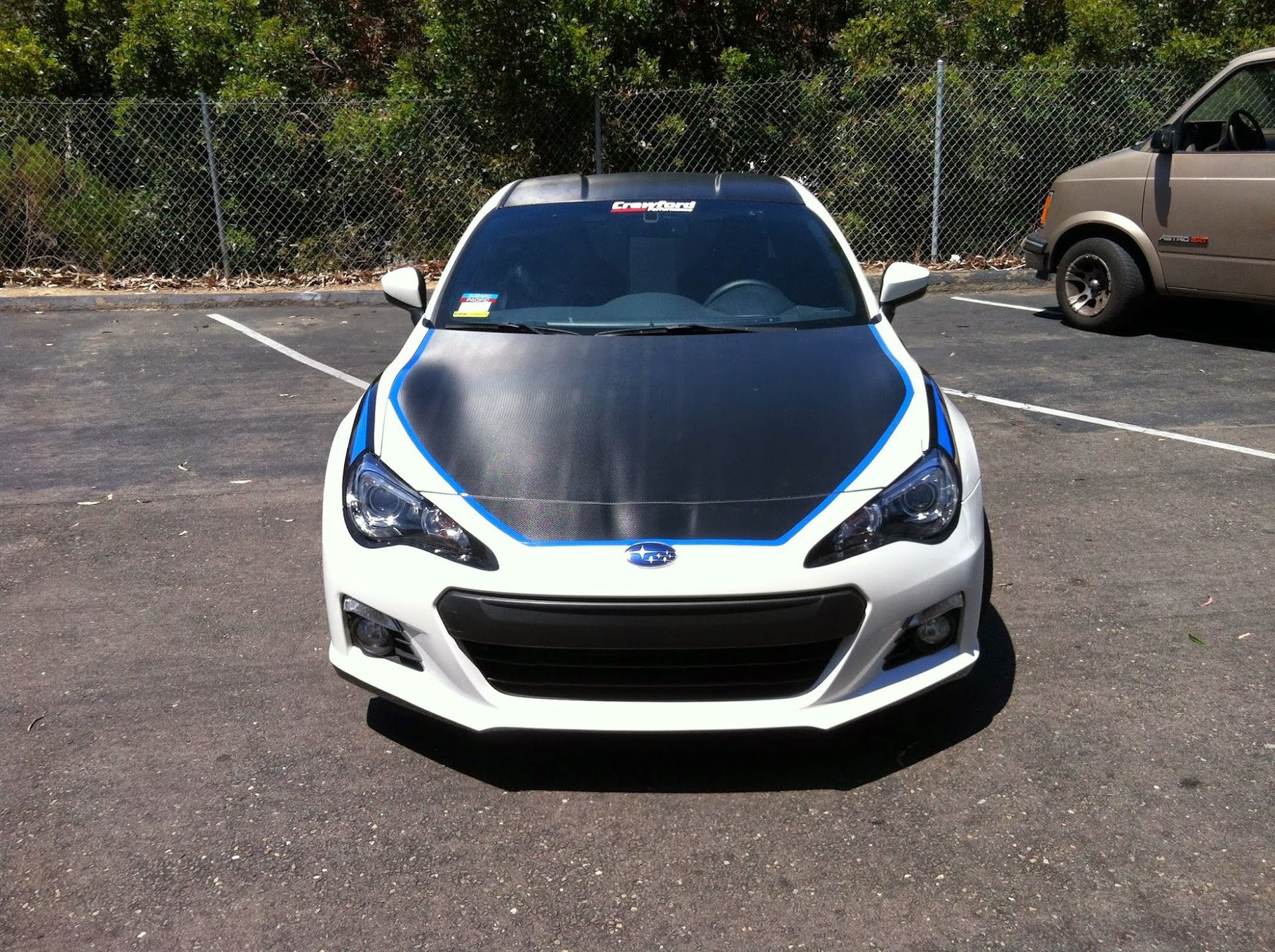 White Subaru BRZ with black hood, blue accents, parked outdoors.
