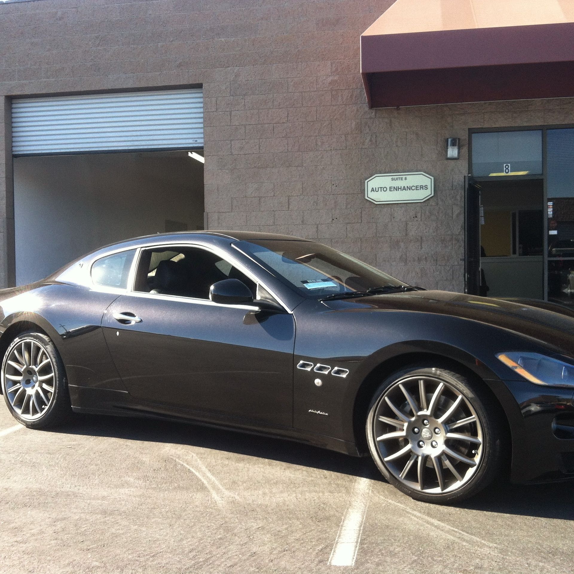 Dark gray Maserati coupe parked outside a business.