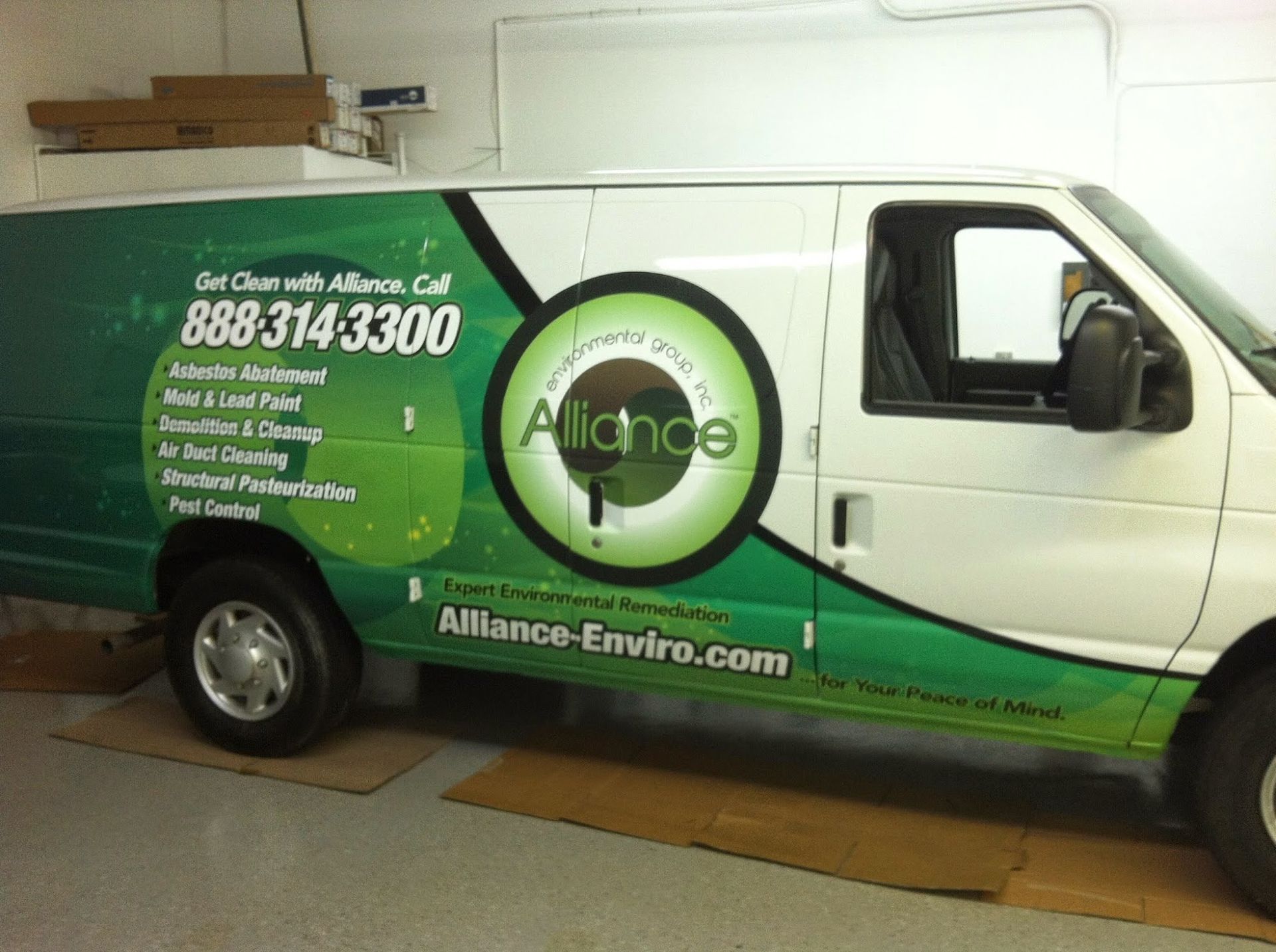 White and green Alliance van parked in a garage, with logo, company info, and website.