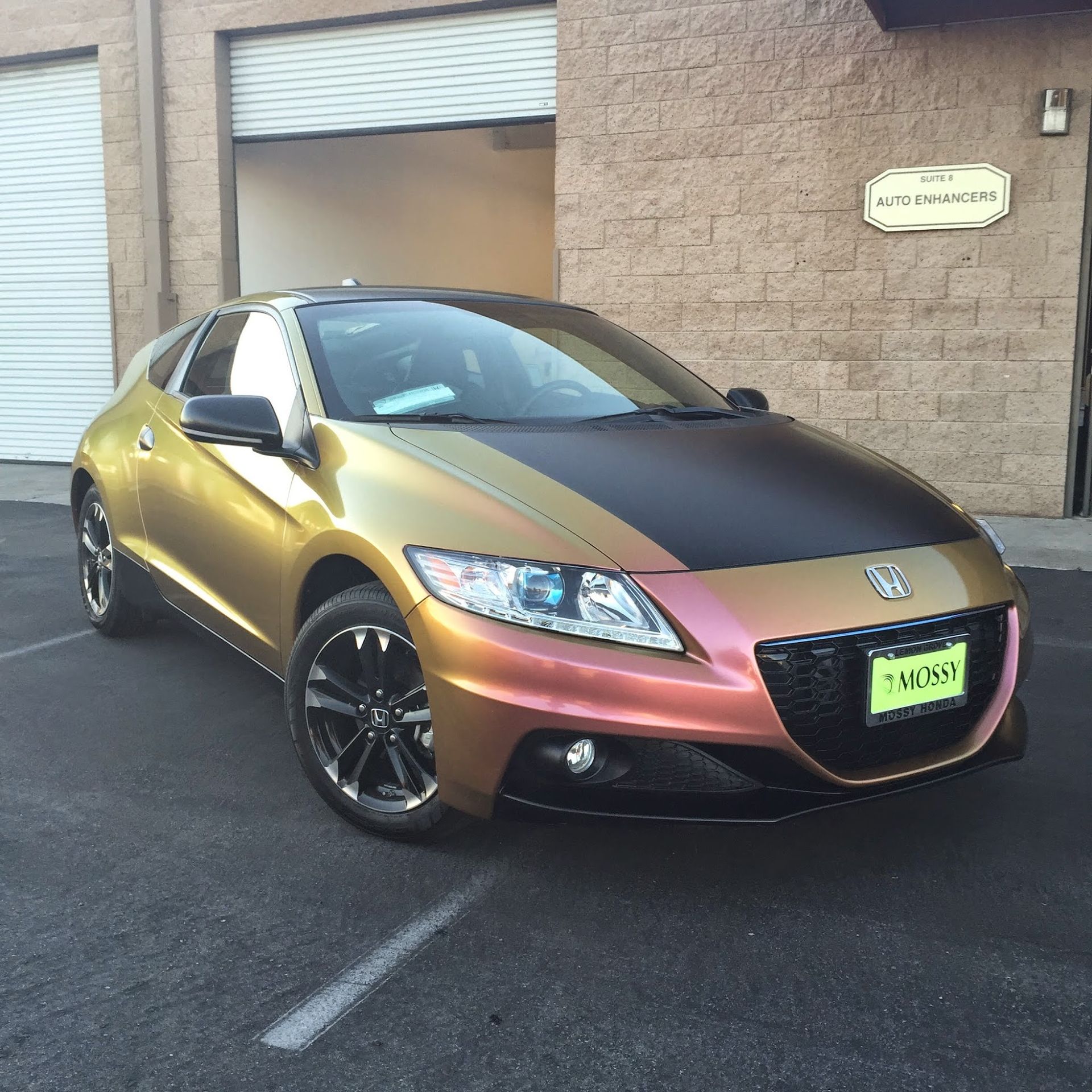 Gold and black Honda CR-Z coupe parked in front of a brick building.