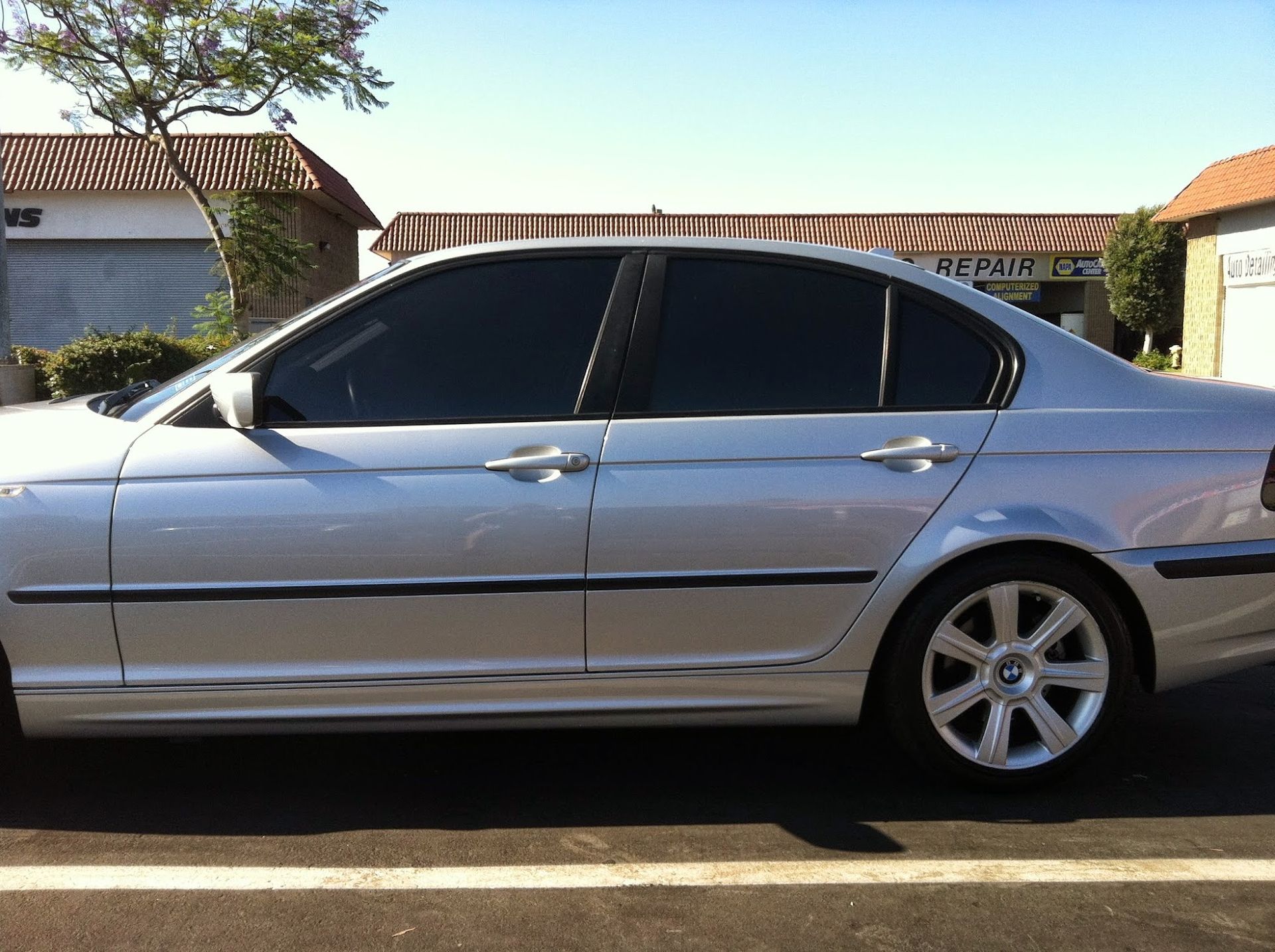 Silver sedan with tinted windows parked in front of a building on a sunny day.
