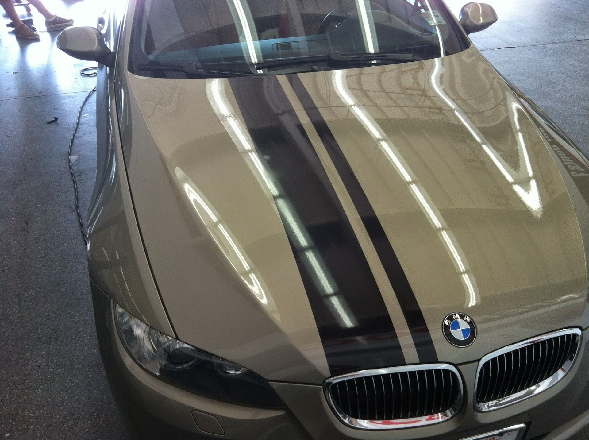 Tan BMW car with black racing stripes, parked under bright lights.