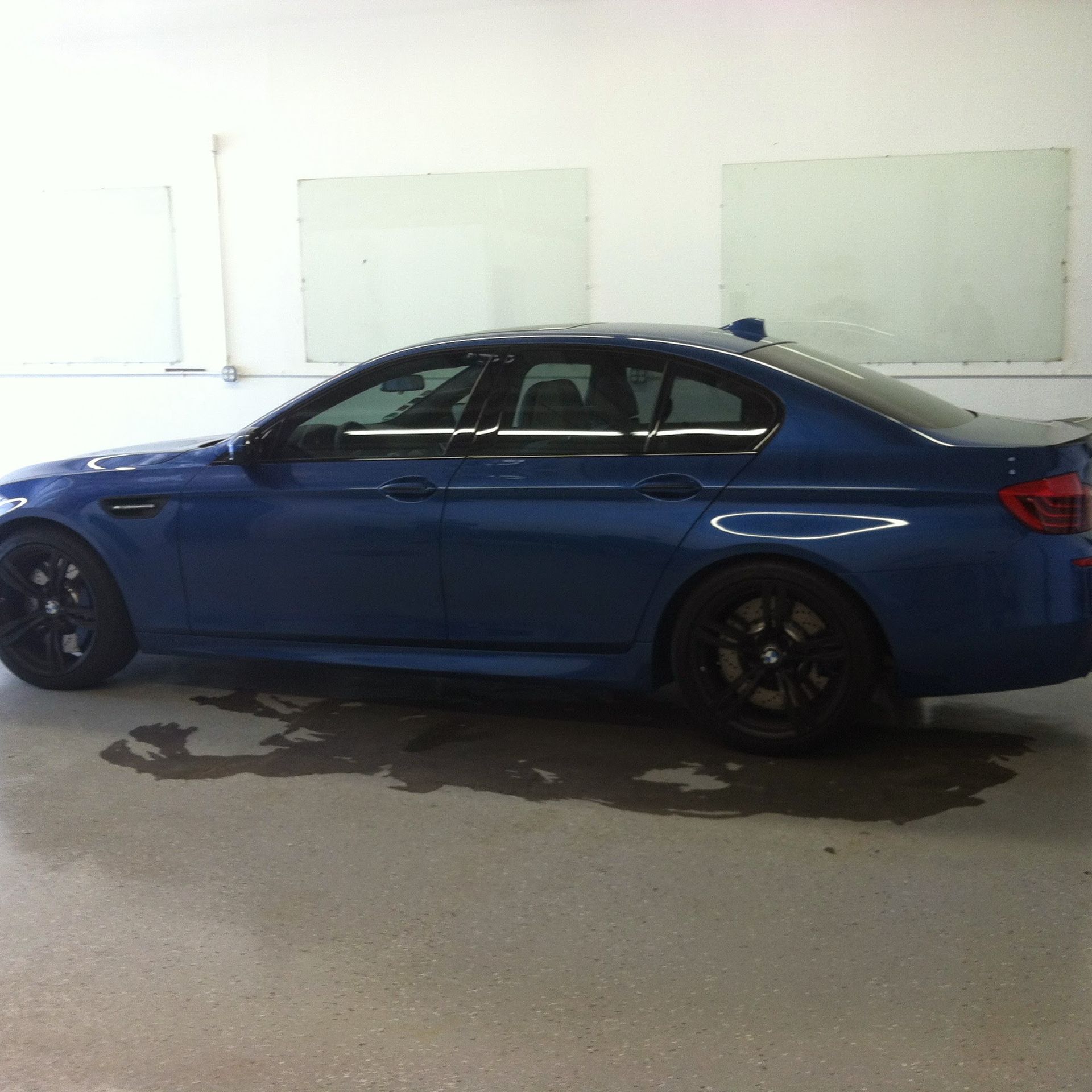 Blue BMW M5 parked indoors, black wheels, wet ground.