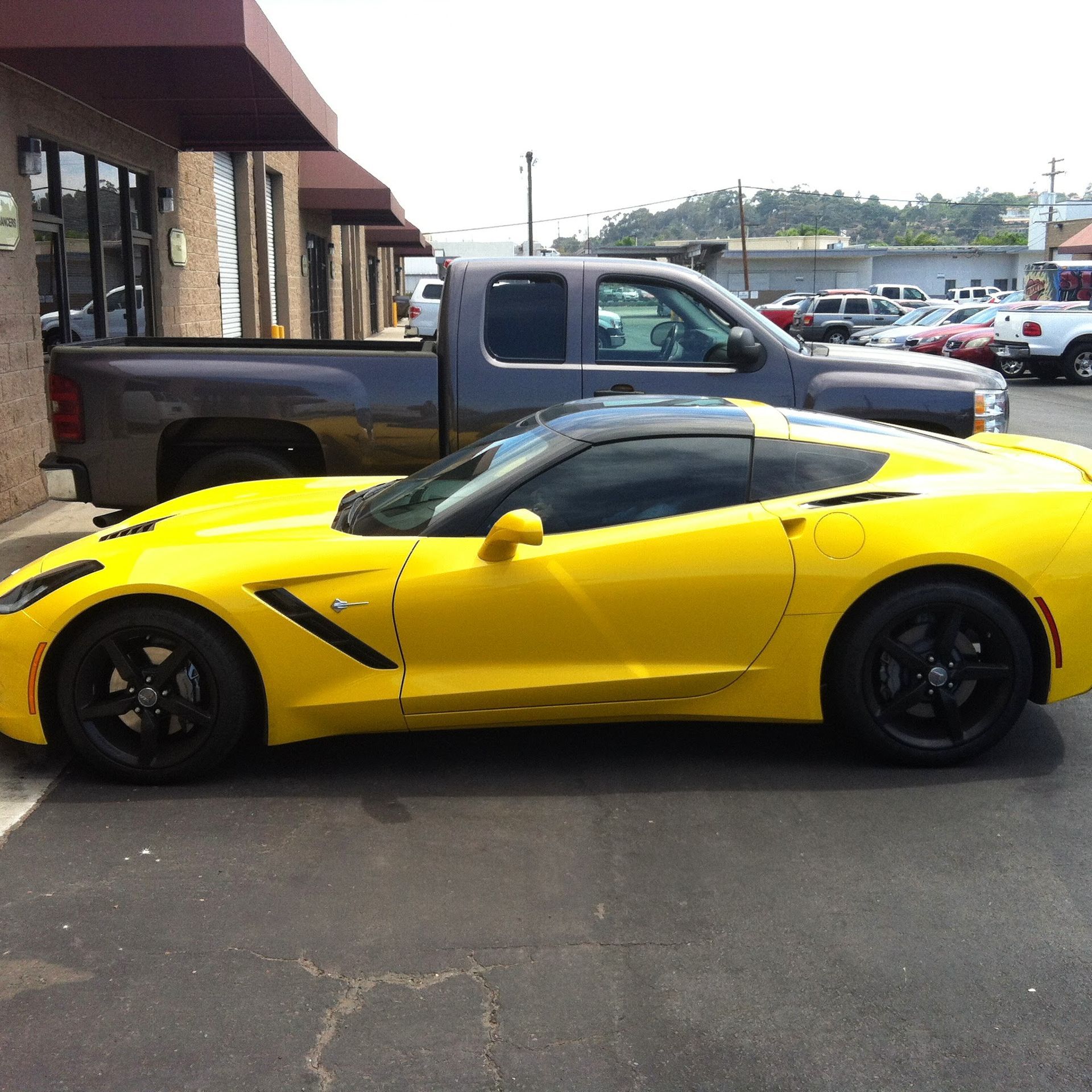 Yellow sports car parked in front of a building; gray pickup truck behind it.