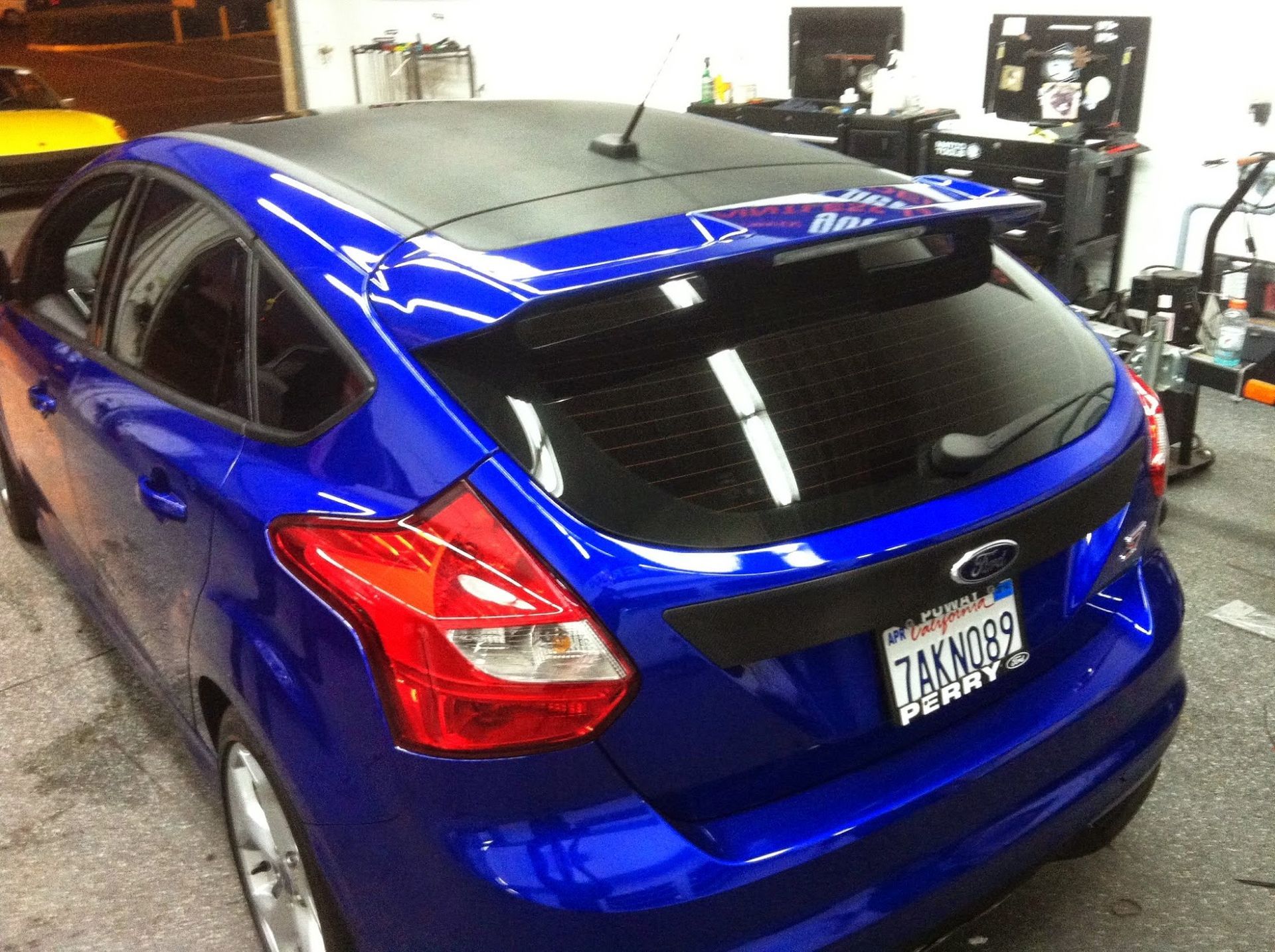 Blue Ford Focus hatchback with a black roof, in a shop setting.