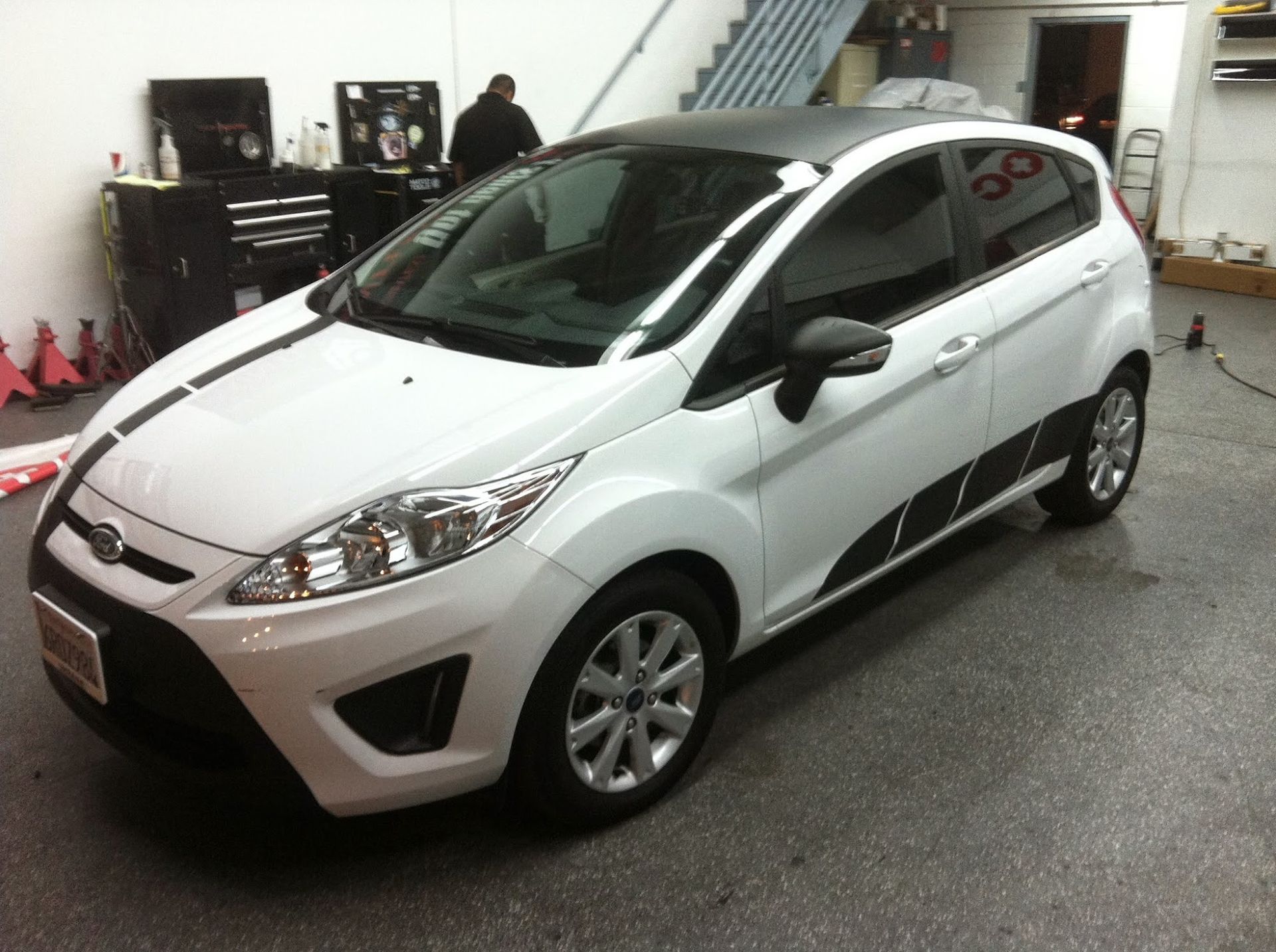 White Ford Fiesta with black racing stripes and roof in a garage.