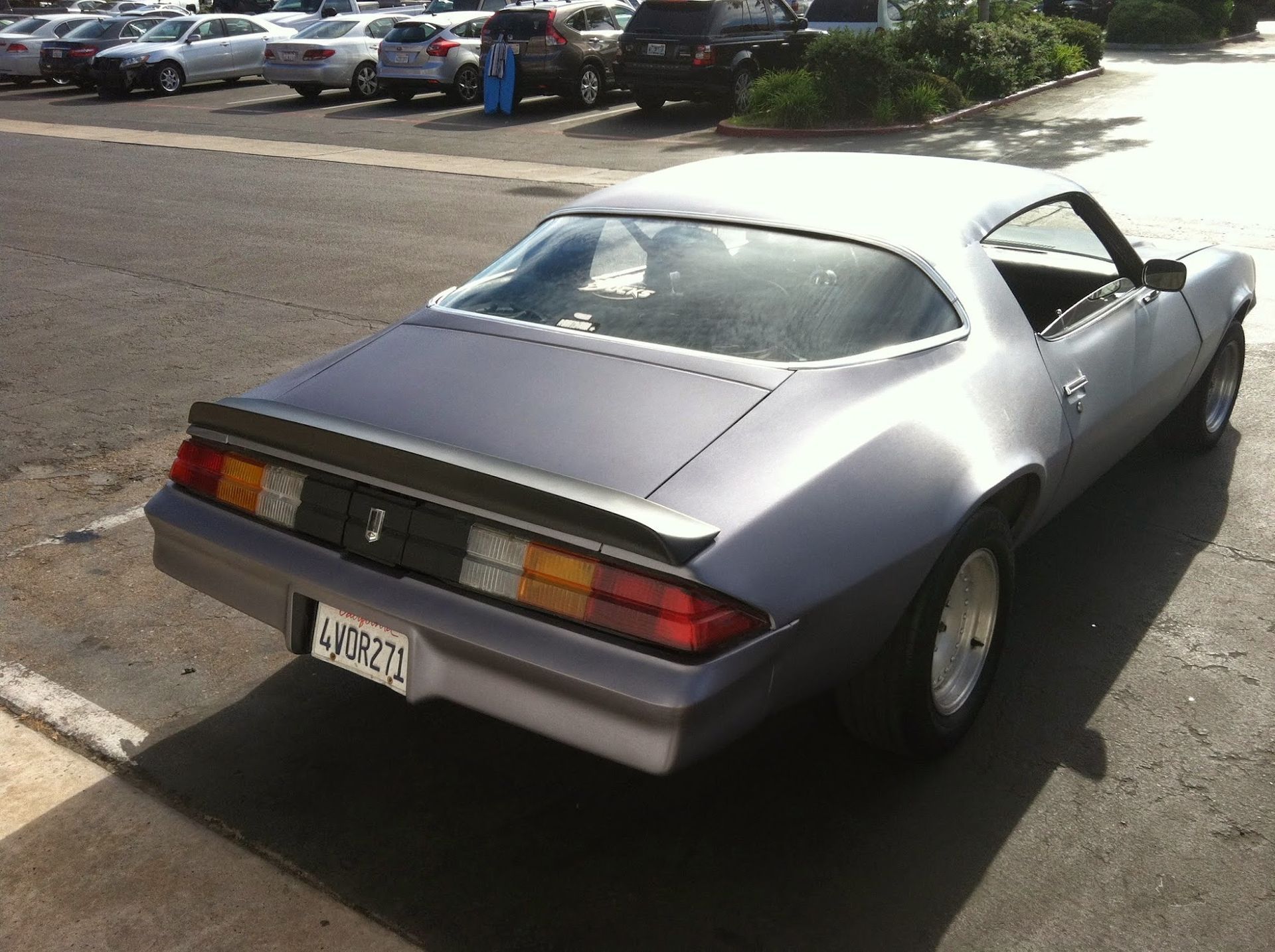 Silver classic Camaro parked in a parking lot with other cars.