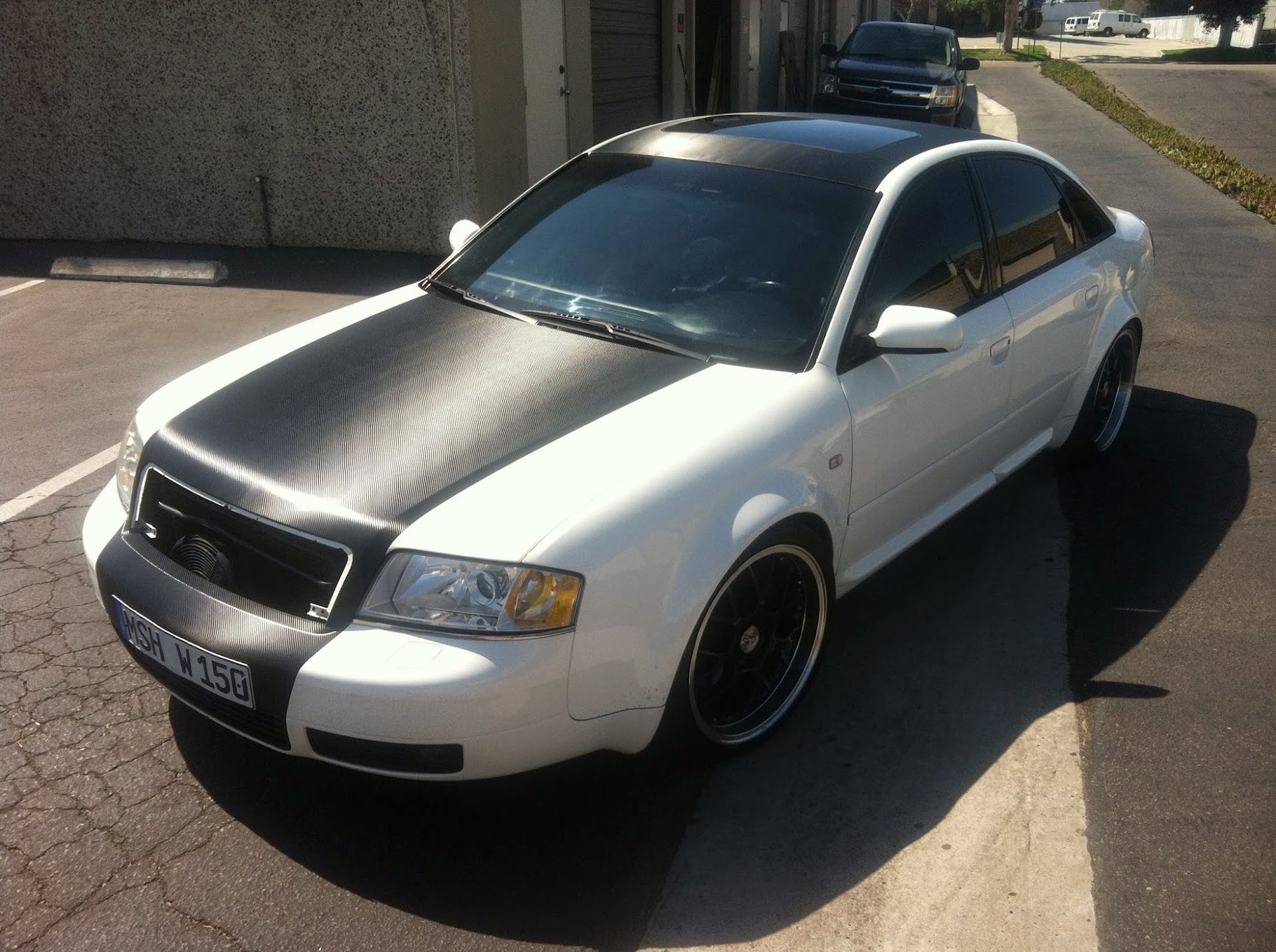 White Audi sedan with black hood, roof, and rims, parked on pavement.
