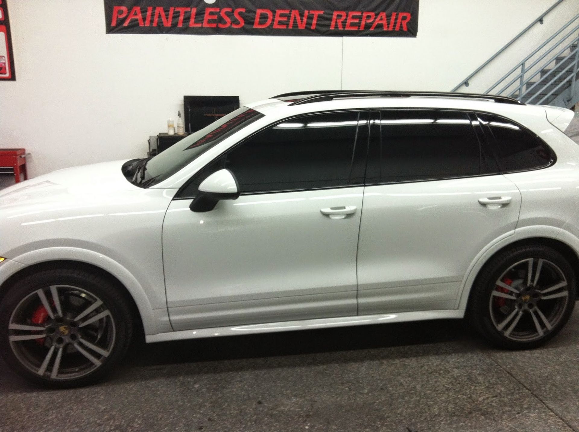 White Porsche SUV with tinted windows inside a paintless dent repair shop.