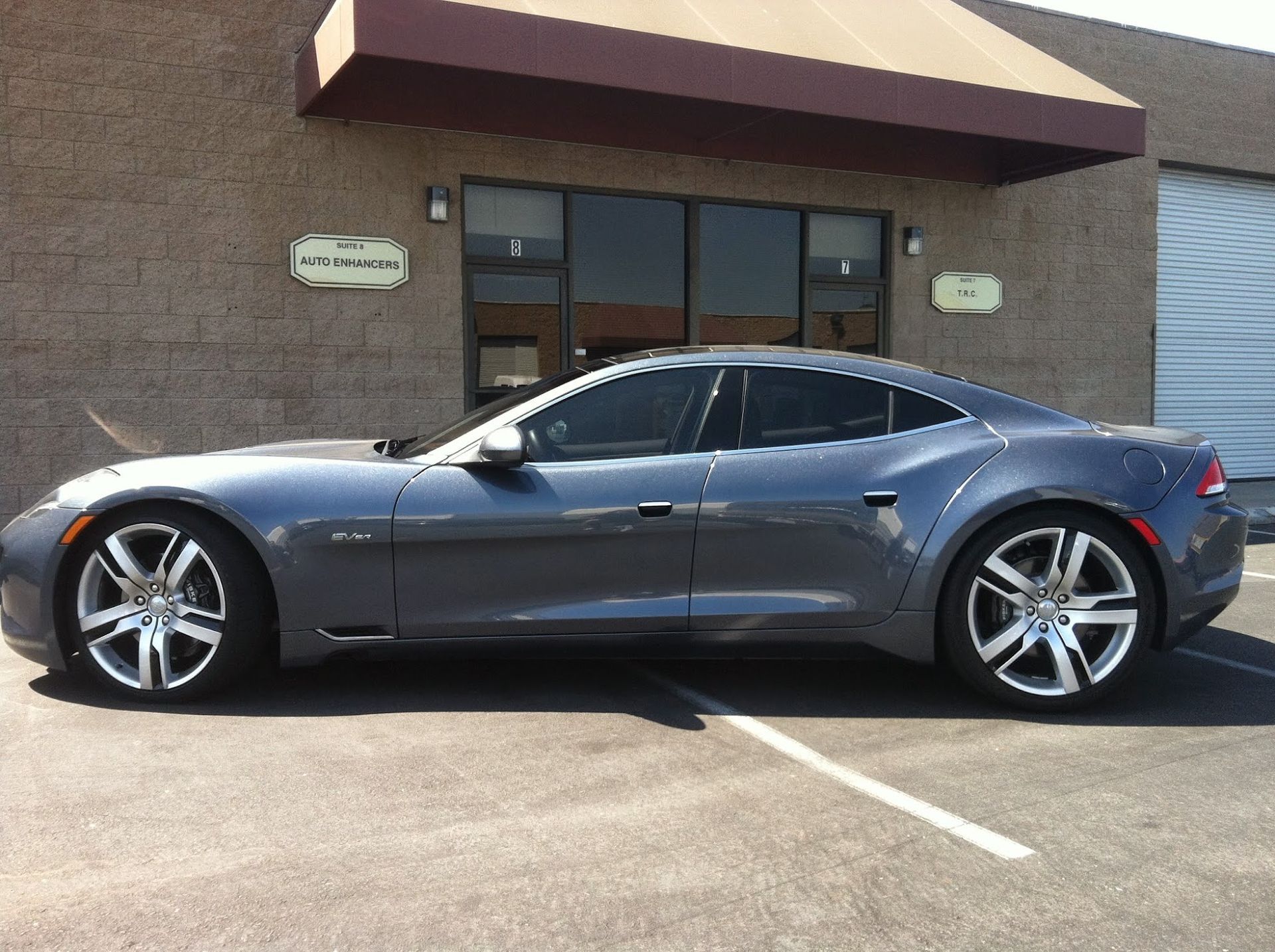 Gray Karma car parked in front of a brick building, with tinted windows and chrome wheels.