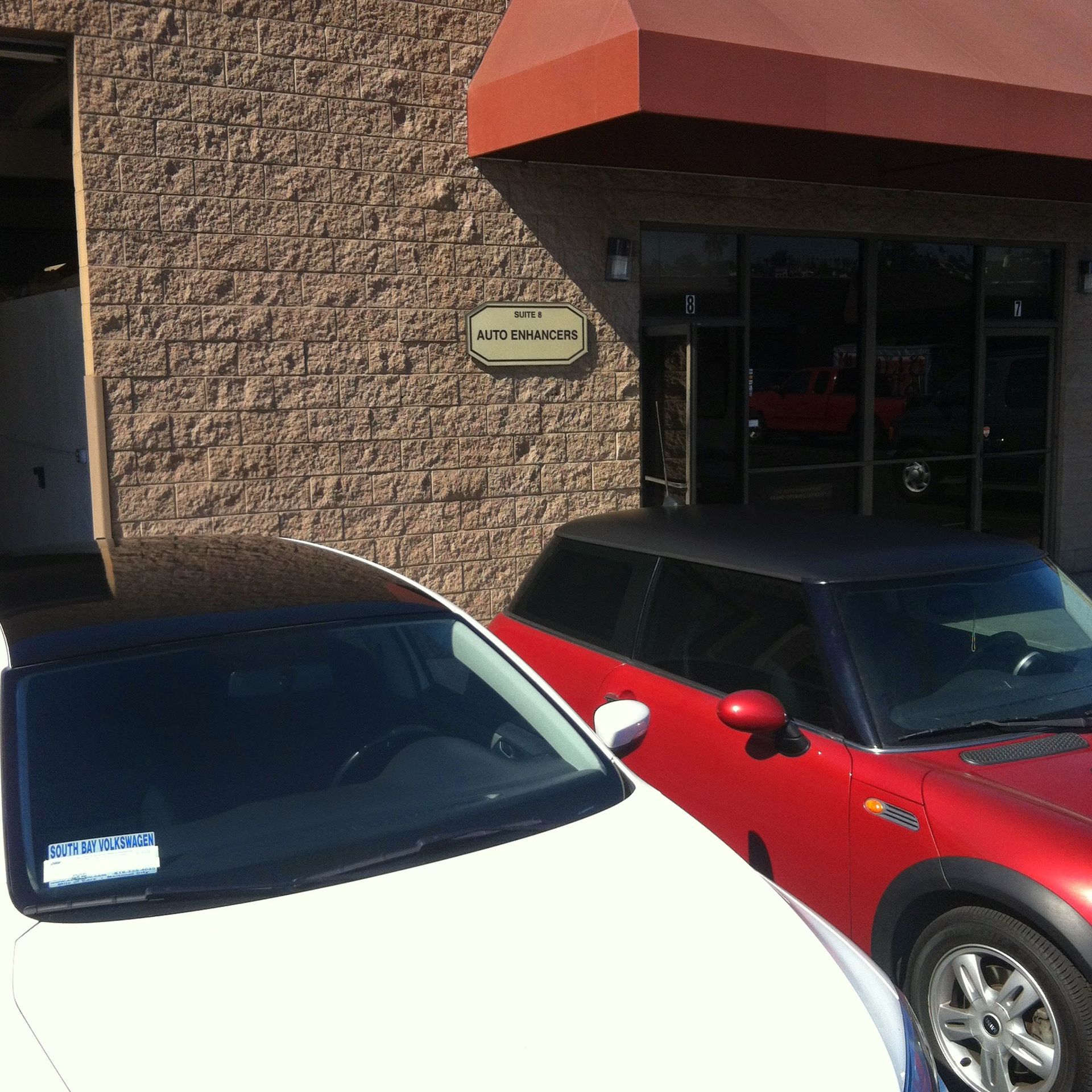 White car parked next to a red Mini Cooper in front of a brick building with glass doors.