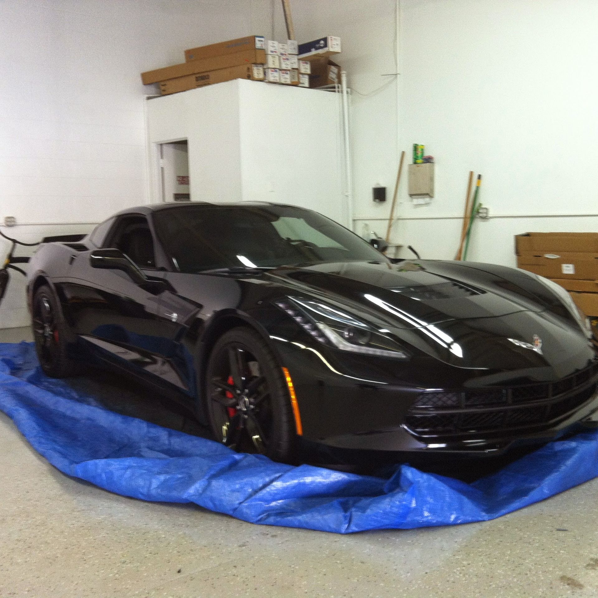 Black Corvette sports car parked on a blue tarp inside a garage.
