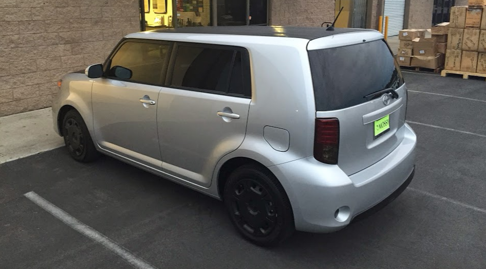 Silver Scion xB with black rims and tinted windows parked near a building.
