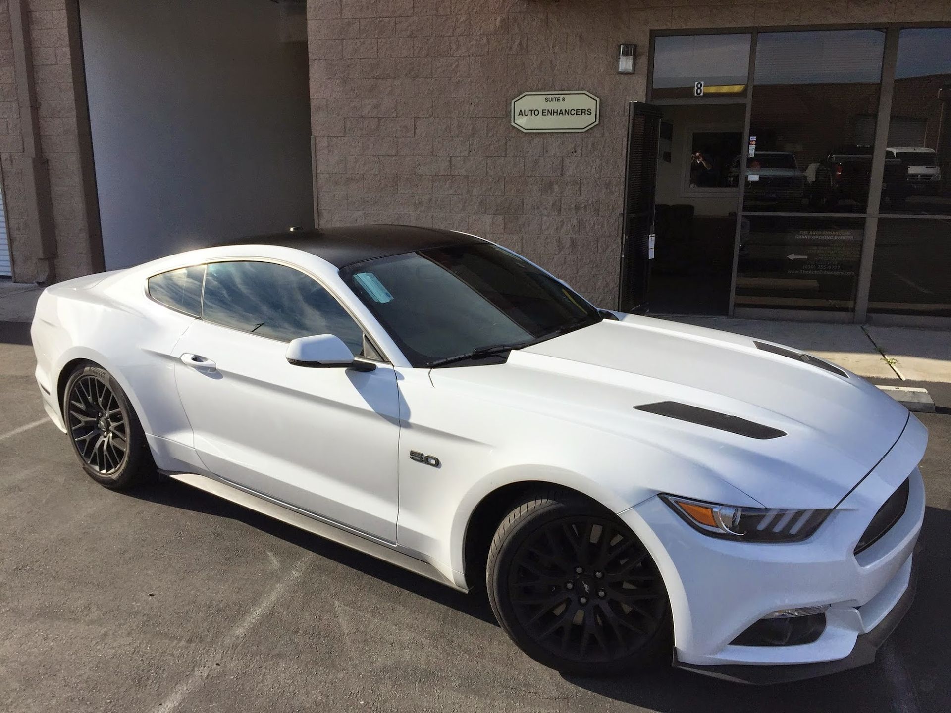 White Ford Mustang with black roof and wheels parked outside a building.