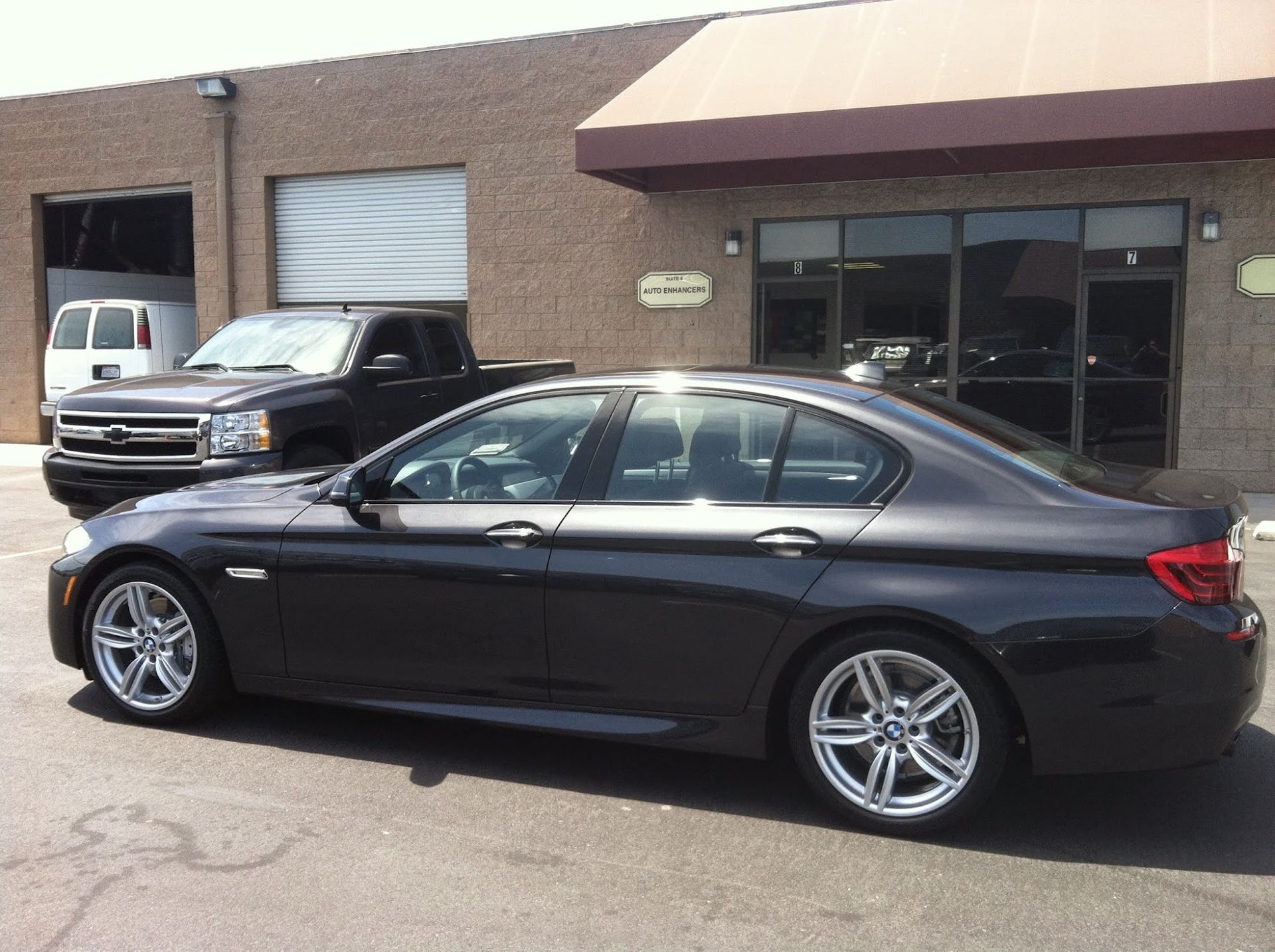 Dark gray BMW sedan parked outside a brick building with a black pickup truck and a white van visible.