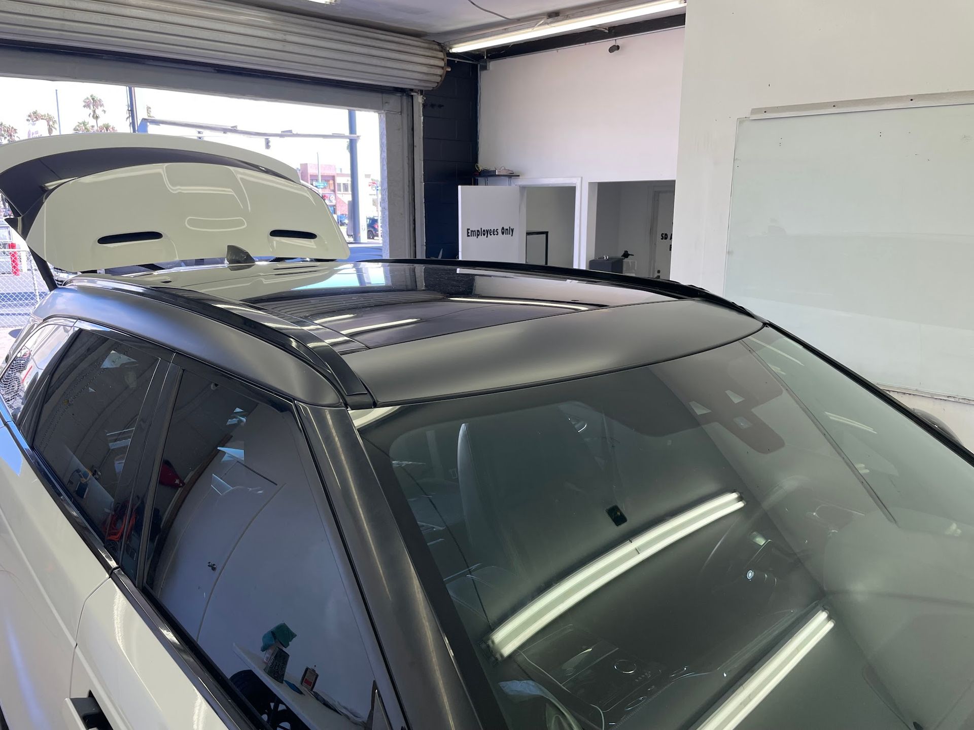 Black-roofed white SUV inside a brightly lit garage, front-end view with the hood and sunroof open.