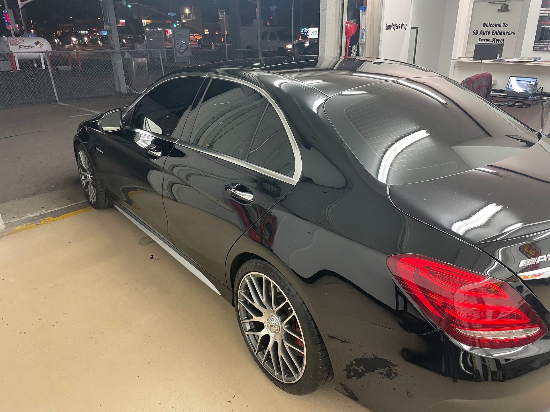 Black Mercedes-Benz sedan with tinted windows, parked outside a shop at night.