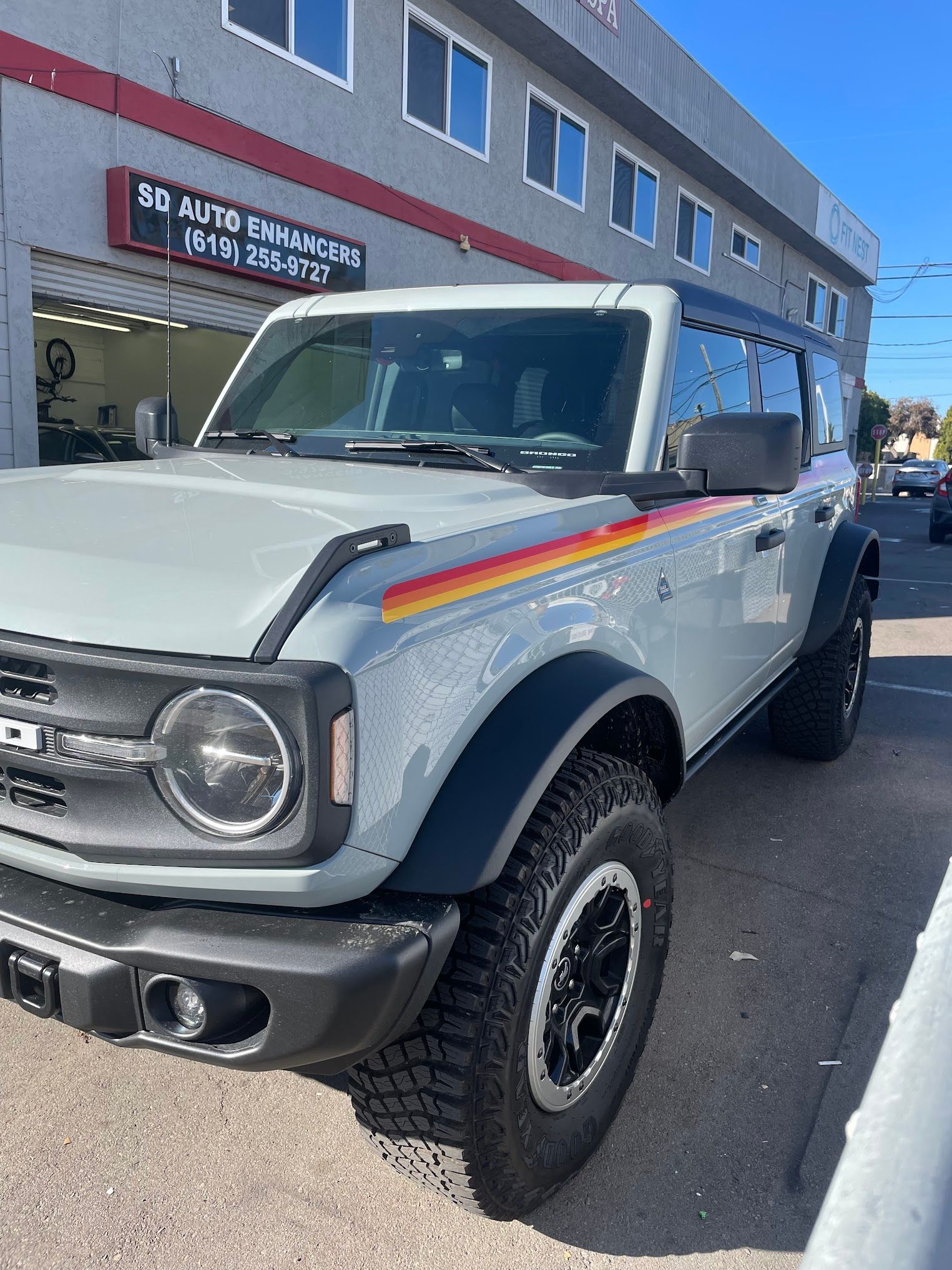 Gray Ford Bronco with retro side stripe parked outside an auto repair shop.