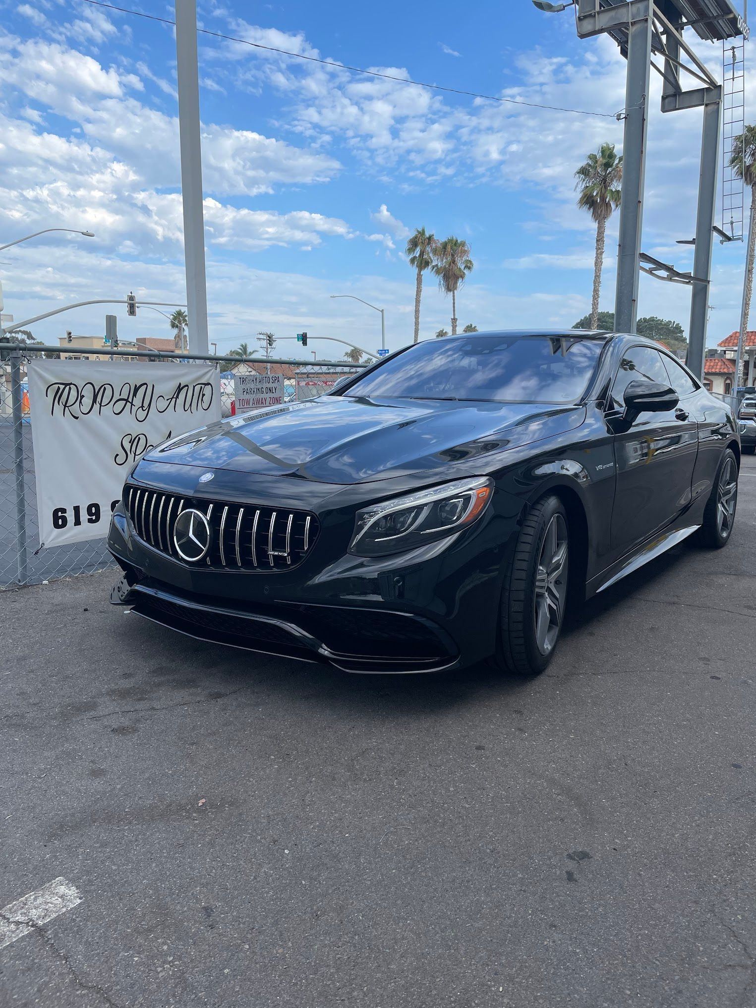 Black Mercedes coupe parked on asphalt, sunny day with palm trees.