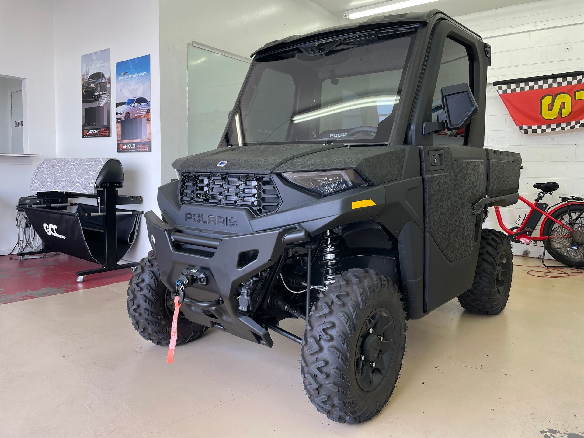 Black Polaris Ranger UTV parked in a garage with a winch and aftermarket bumper.