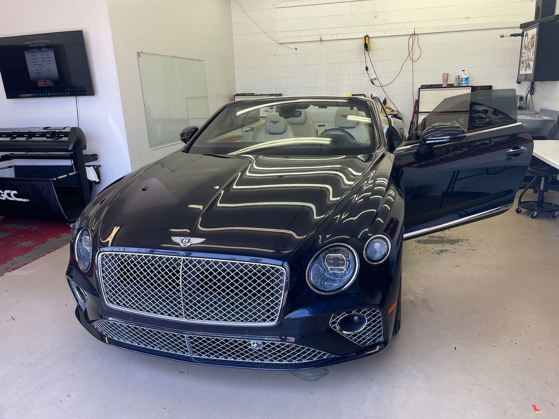 Dark blue Bentley convertible with door open in a workshop.