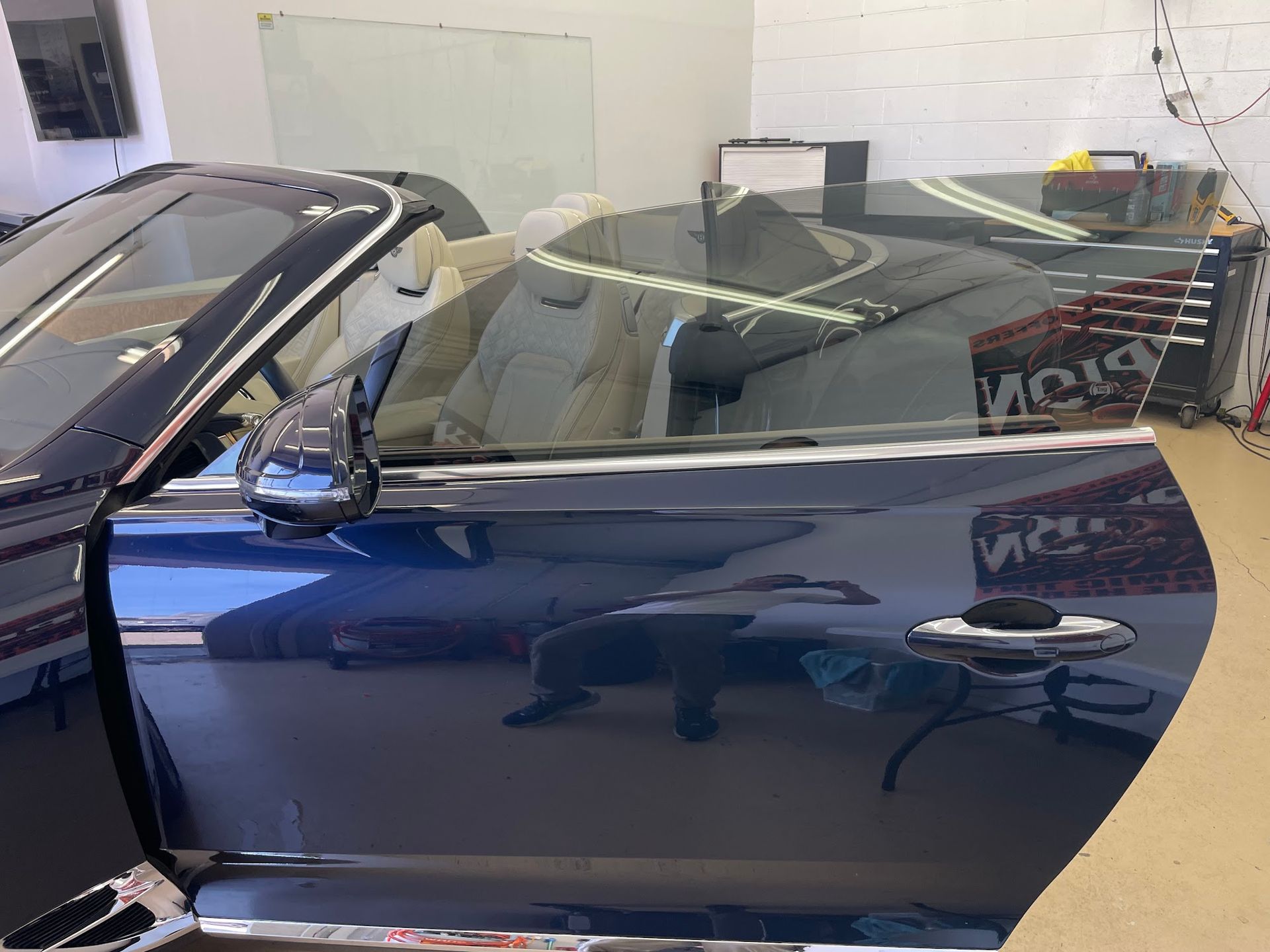 Blue convertible car door open; tan interior. Reflective glass window.