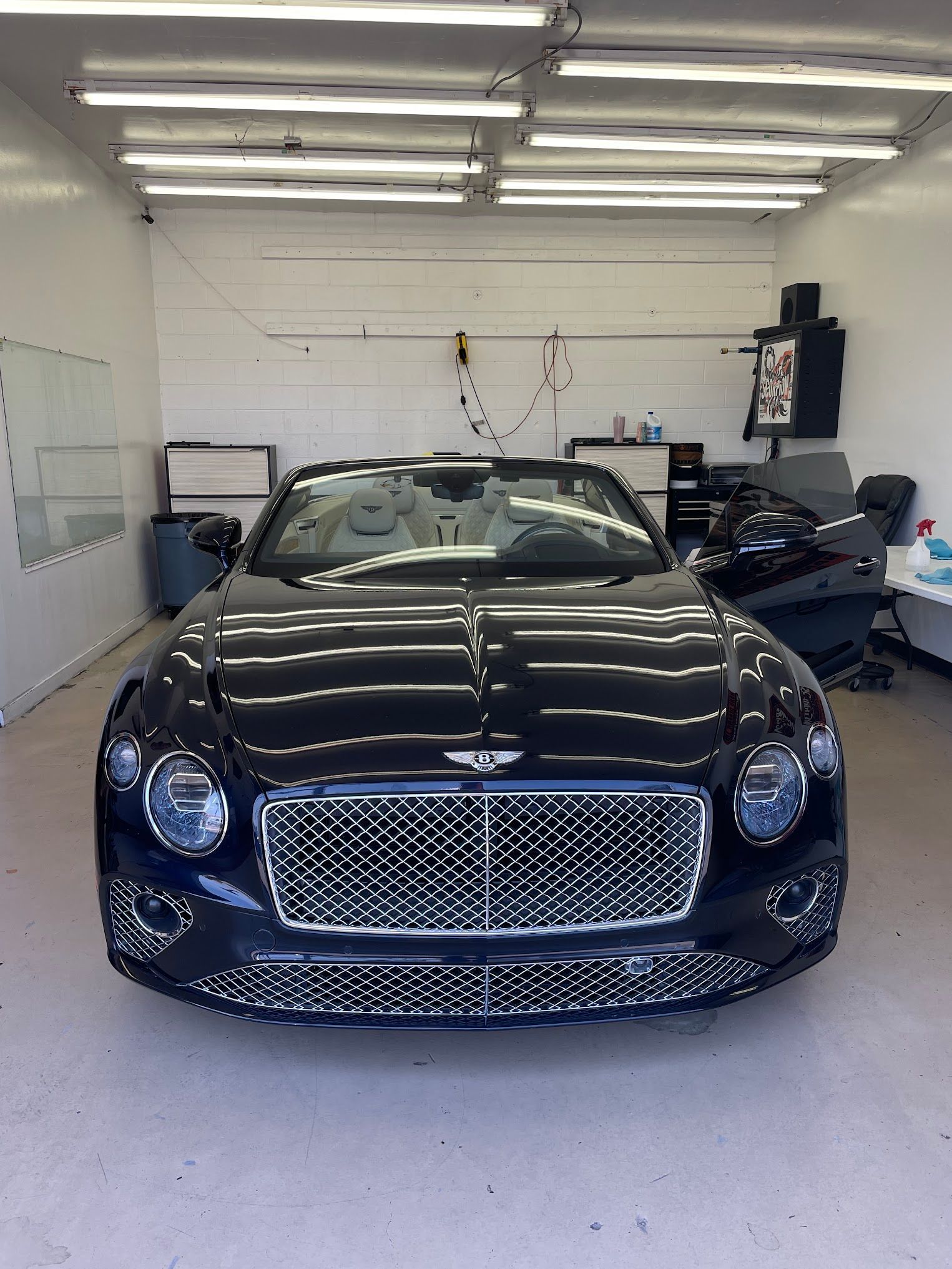 Dark blue Bentley convertible parked inside a brightly lit garage.
