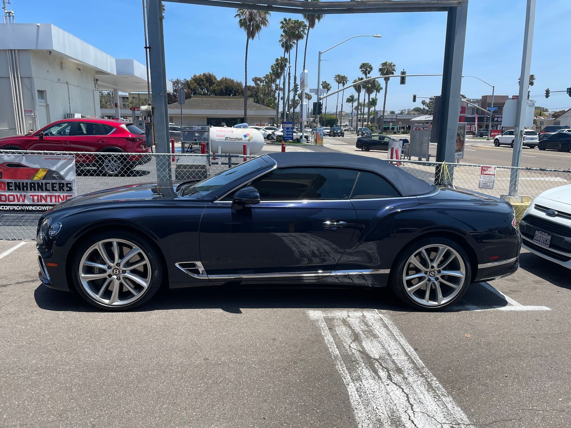 Dark blue Bentley convertible parked near a car wash, with palm trees in the background.