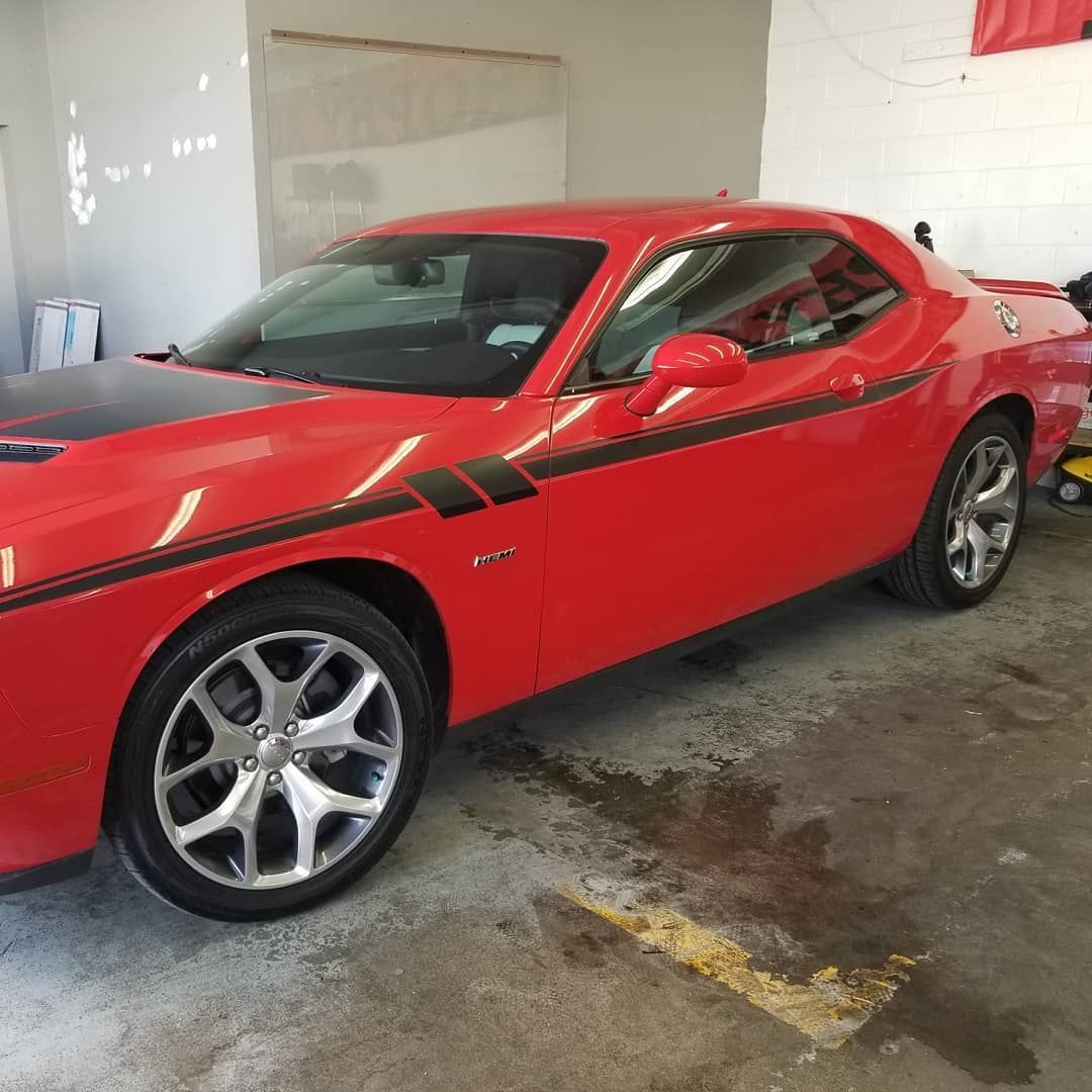 Red Dodge Challenger with black racing stripe, parked in a garage.