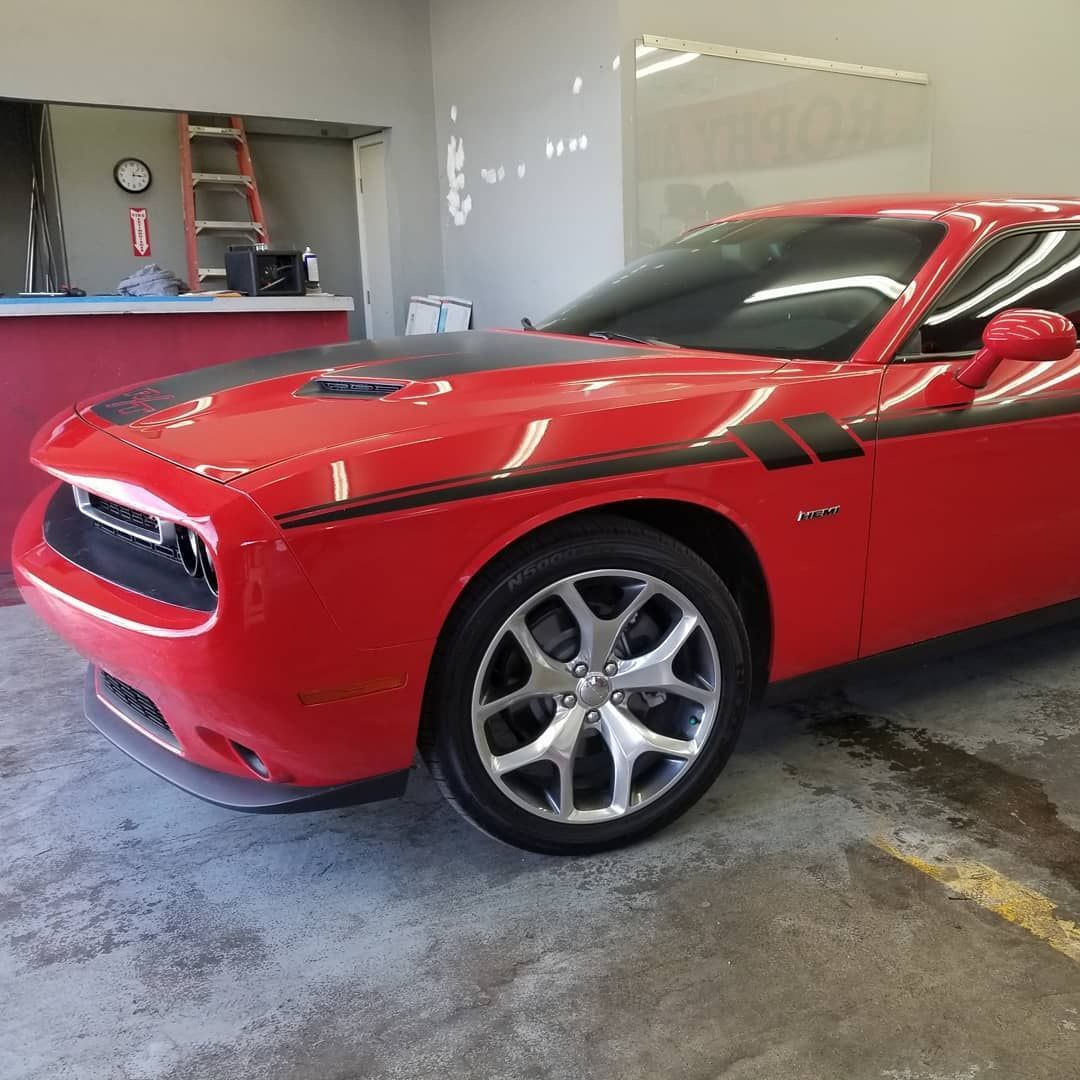 Red Dodge Challenger sports car with black stripes parked inside a building.